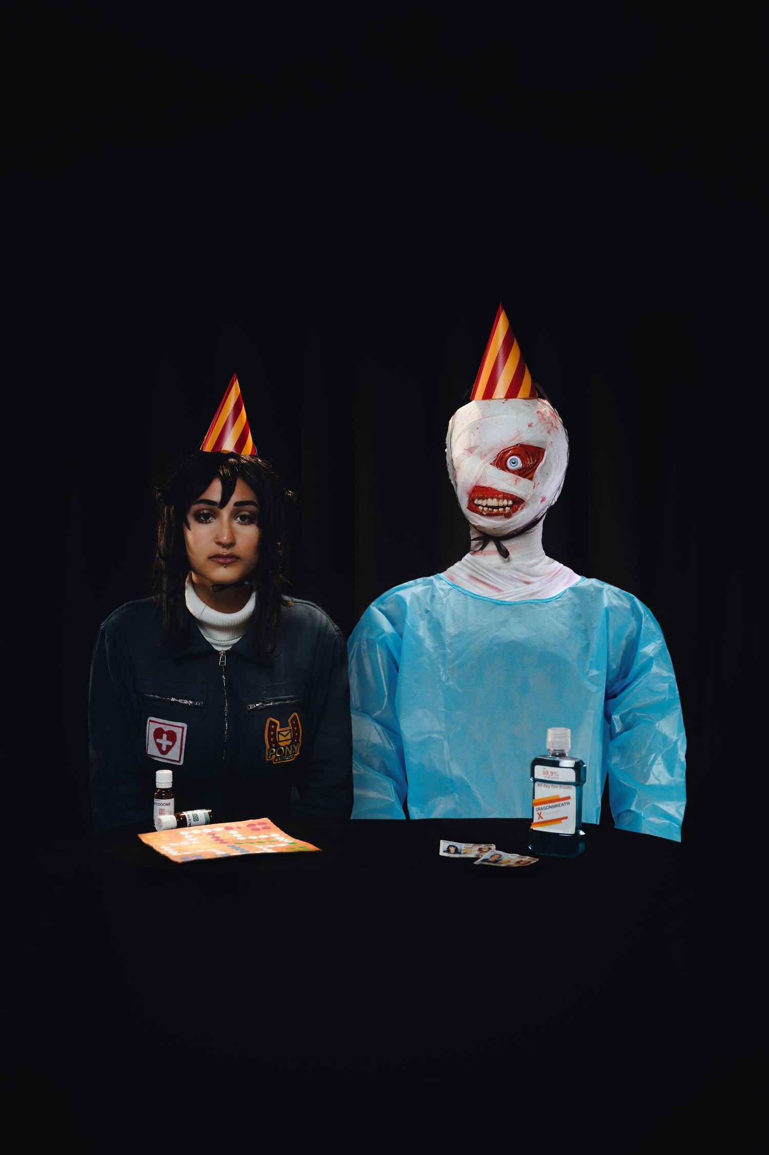 Two people sitting side by side in dark setting with one wearing a black jacket and one in light blue medical scrubs.