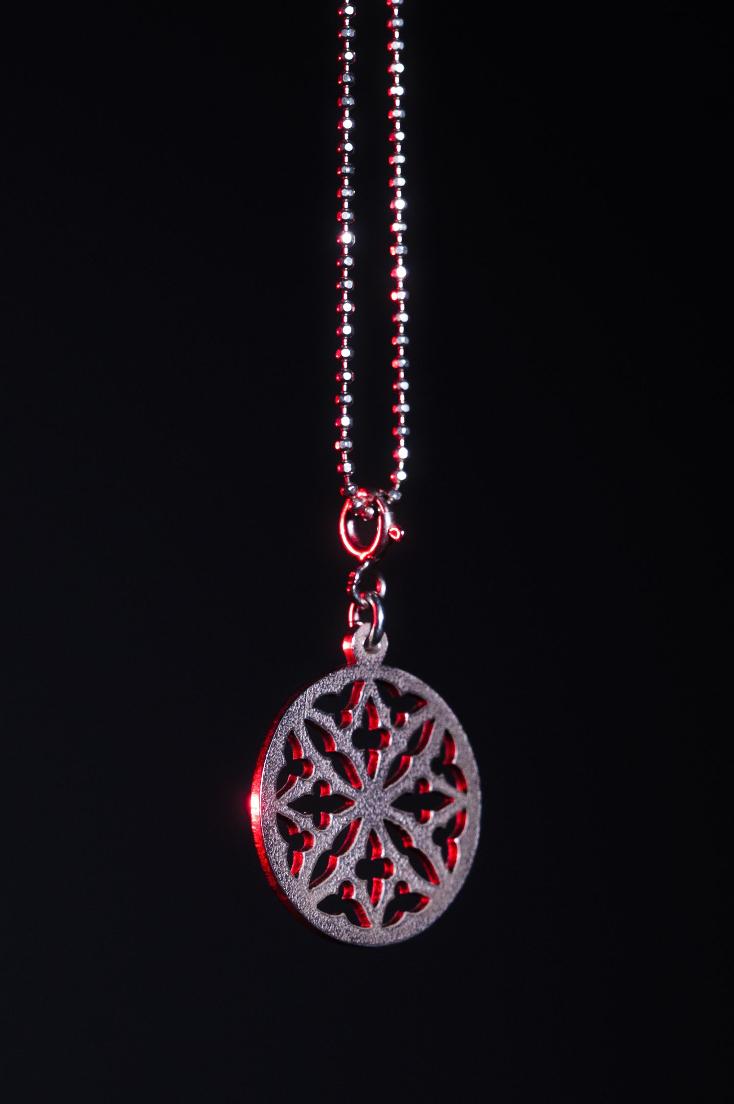 Red and silver filigree oval pendant necklace with ball chain on black background.