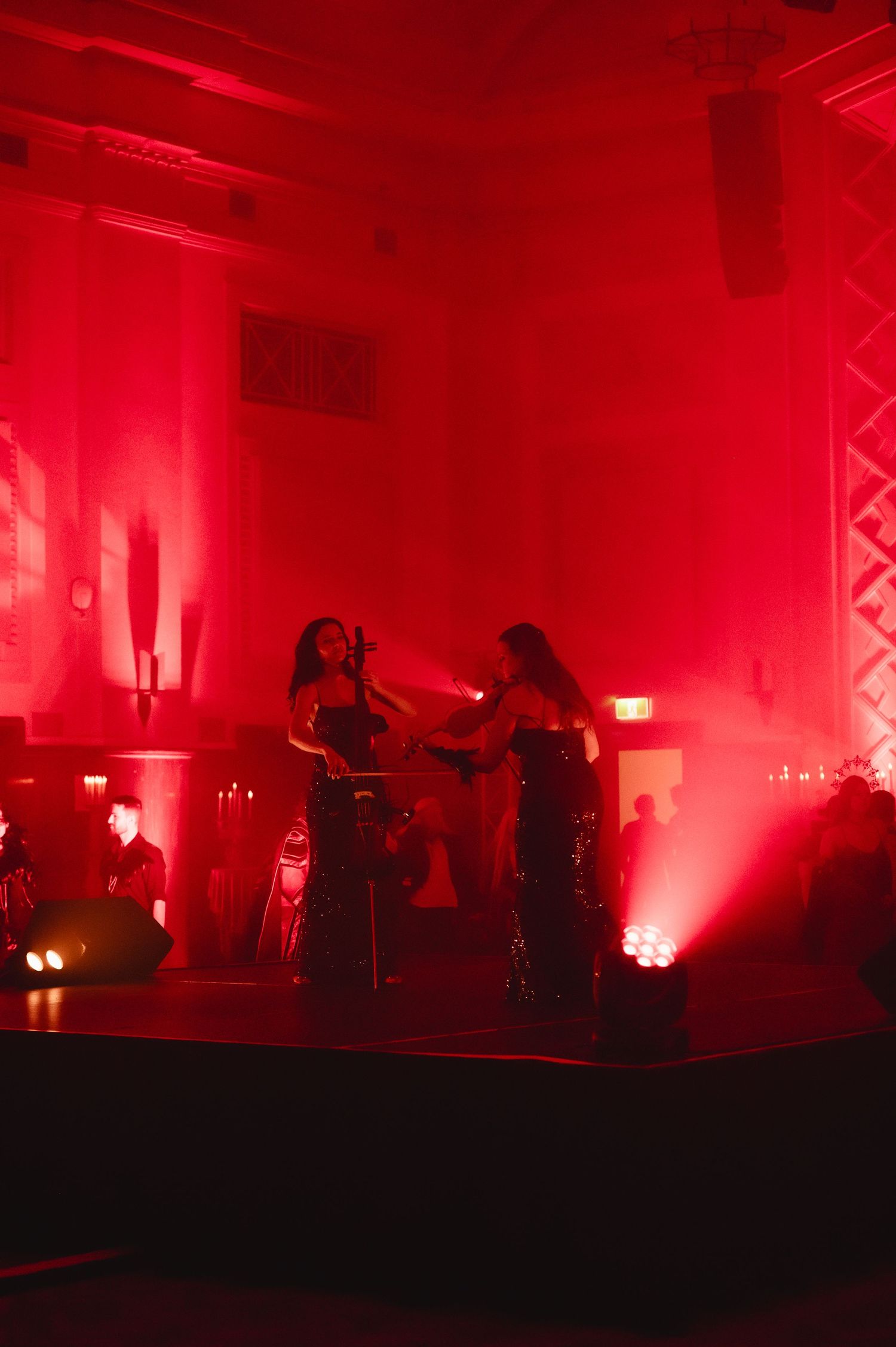 Two performers on stage bathed in dramatic red lighting during a live music event in an ornate venue.