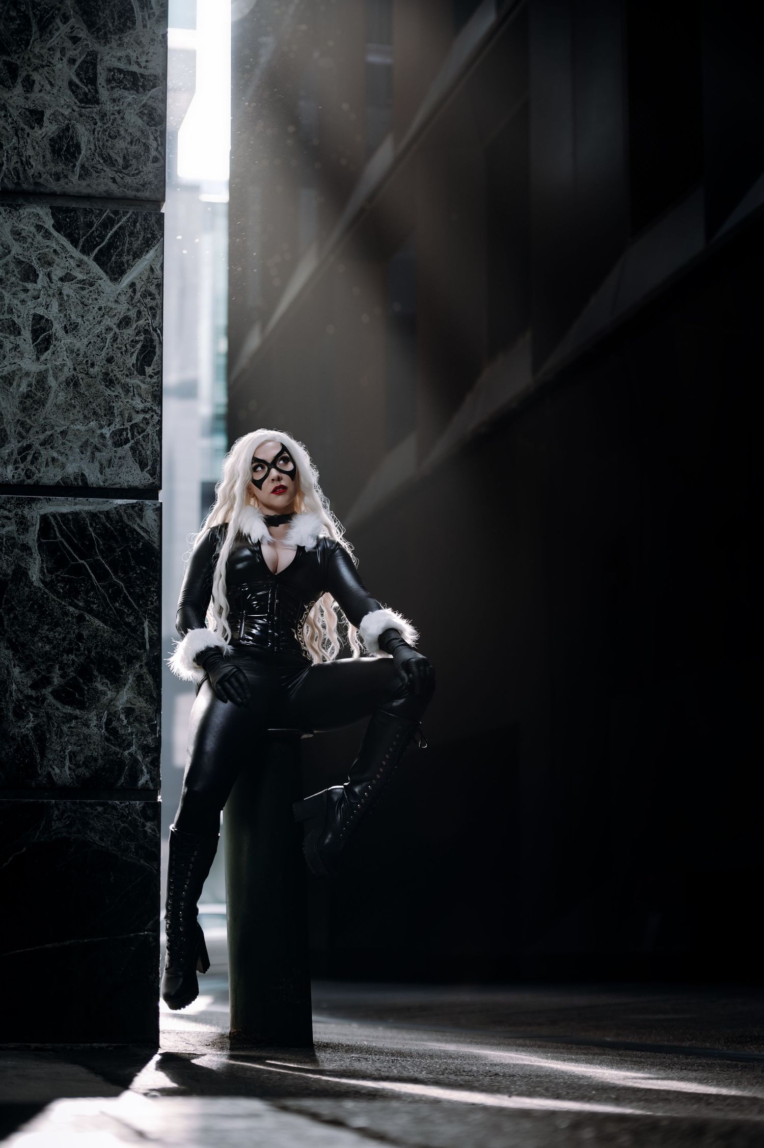 Moody portrait of a cosplayer in black attire standing in dramatic lighting against stone walls.