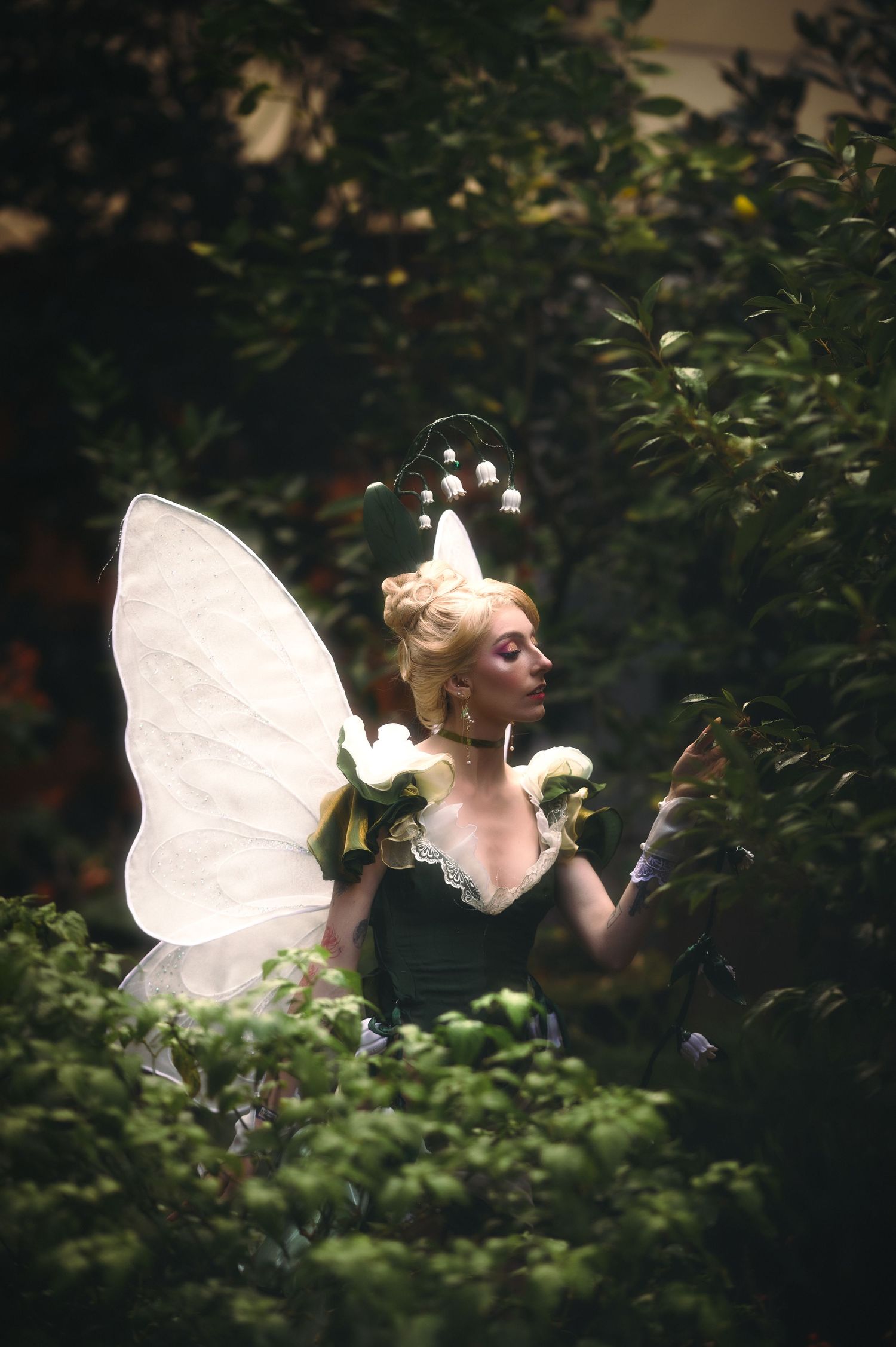 Whimsical fairy character with luminous wings posed in garden greenery.