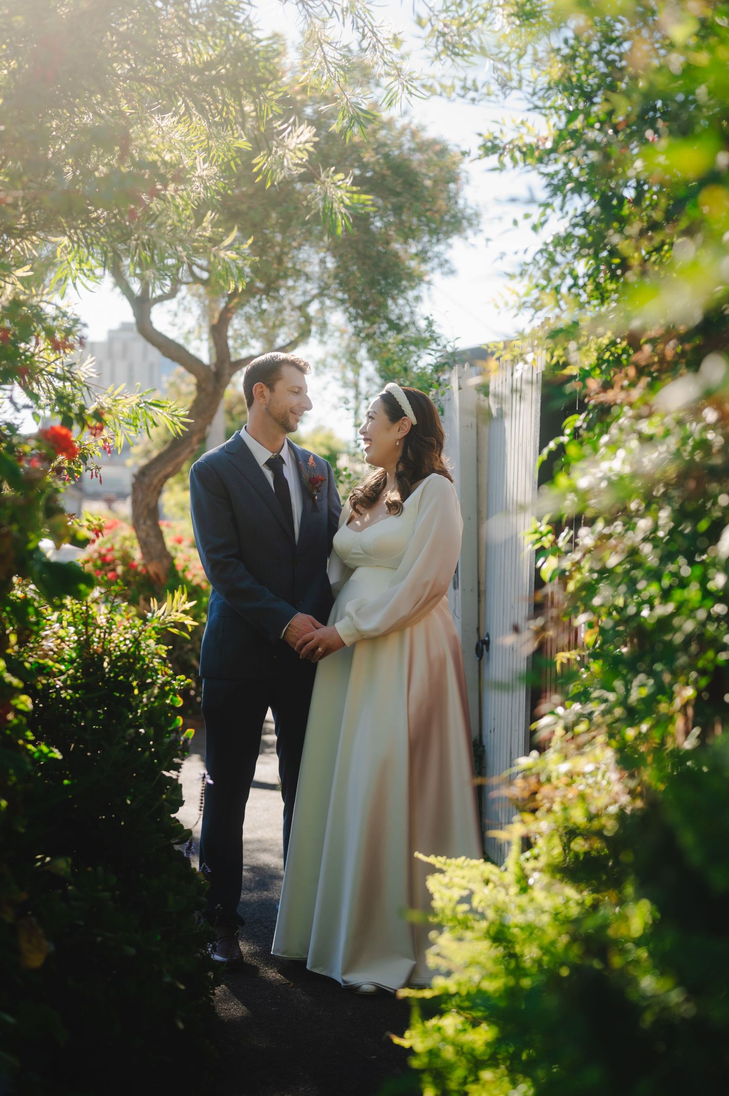 A couple shares a romantic moment in a lush garden setting with sunlight filtering through green foliage.