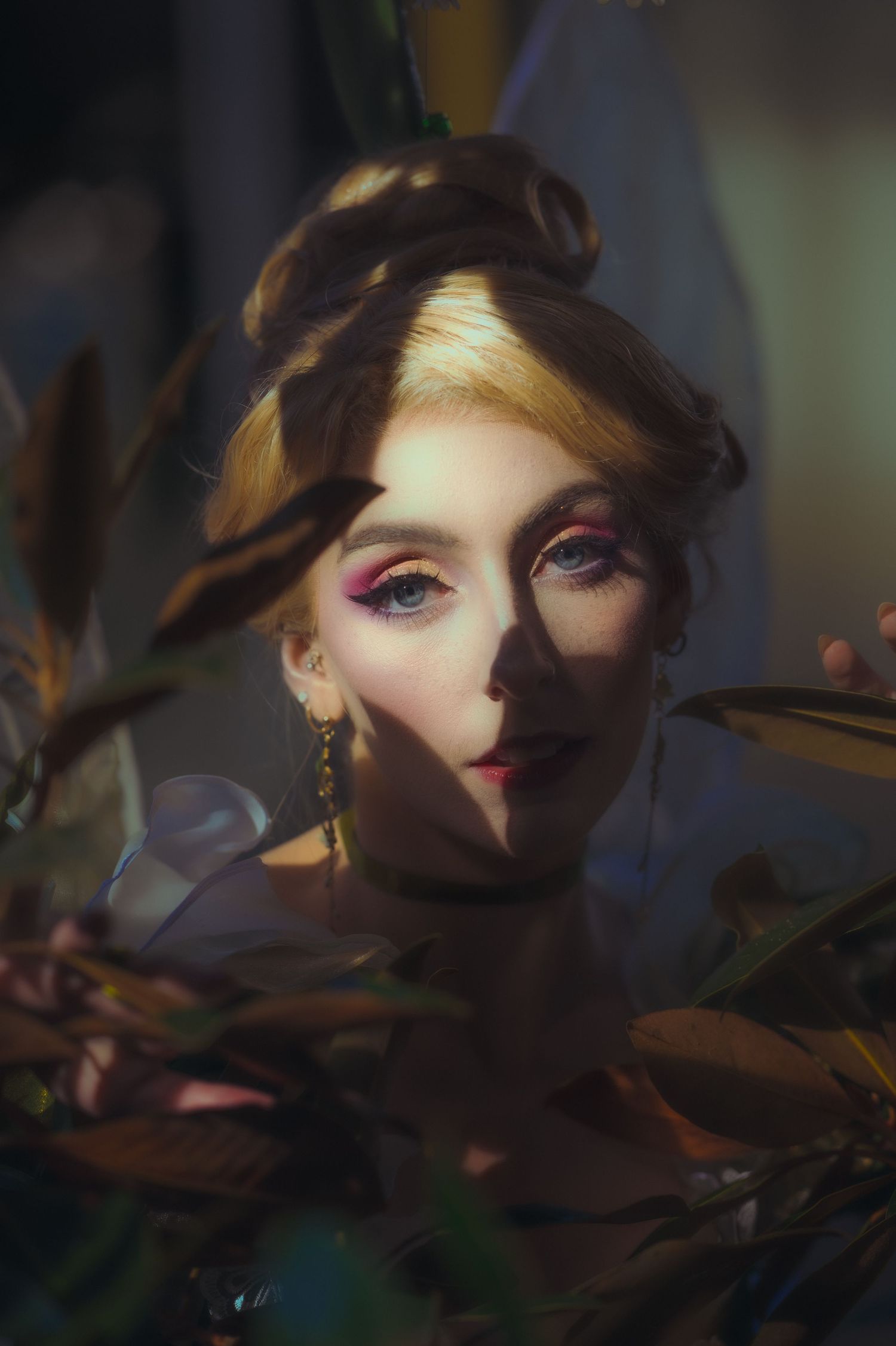 Dramatic portrait with purple eye makeup and moody lighting among leaves.