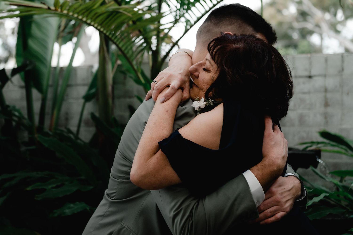 Wedding couple shares an intimate moment surrounded by tropical greenery in a romantic outdoor setting.