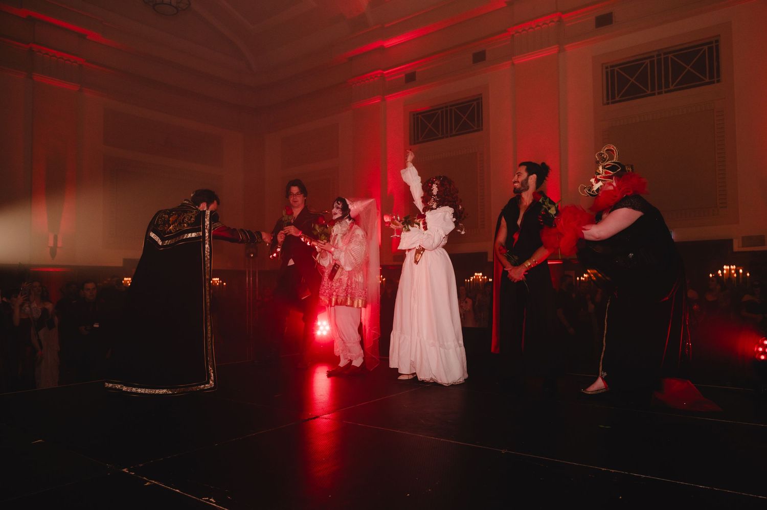 A dark room illuminated with red lighting shows silhouettes of people dancing at what appears to be a wedding reception.