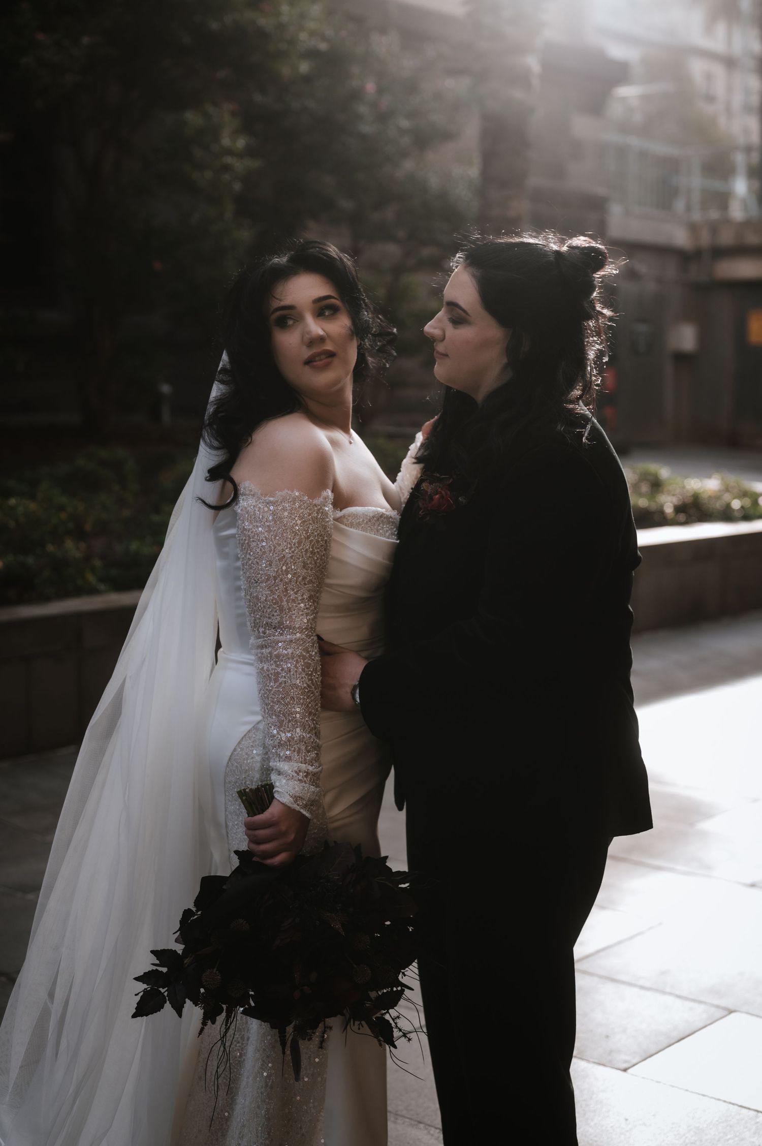 A romantic wedding photoshoot featuring a couple in formal attire against a stone building backdrop.