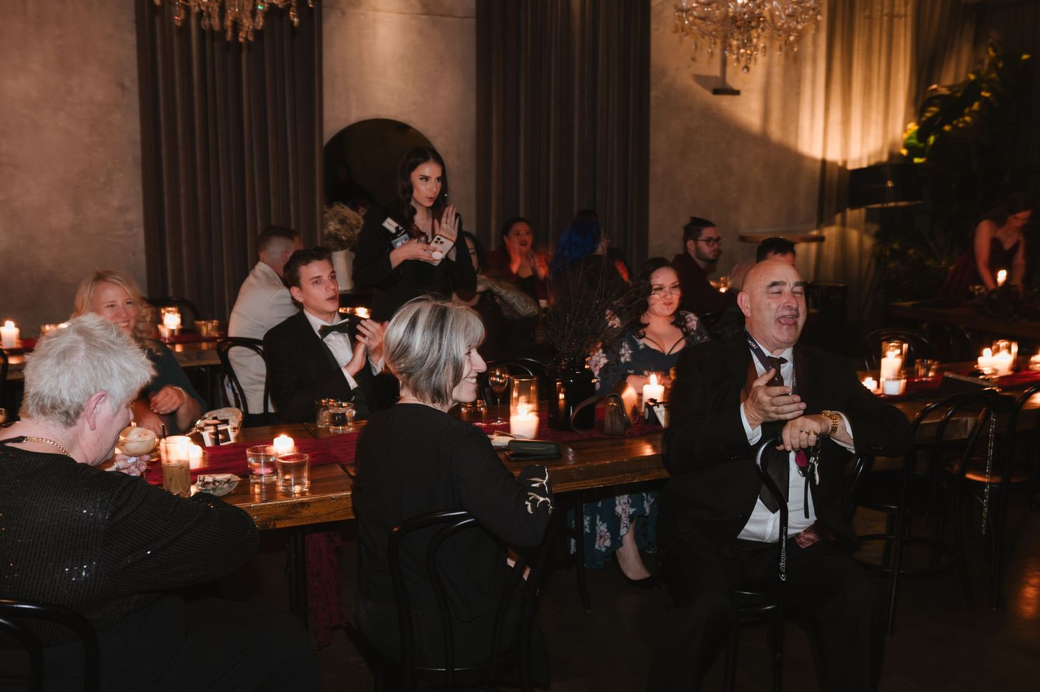 Dimly lit reception hall with guests seated at tables under crystal chandeliers.