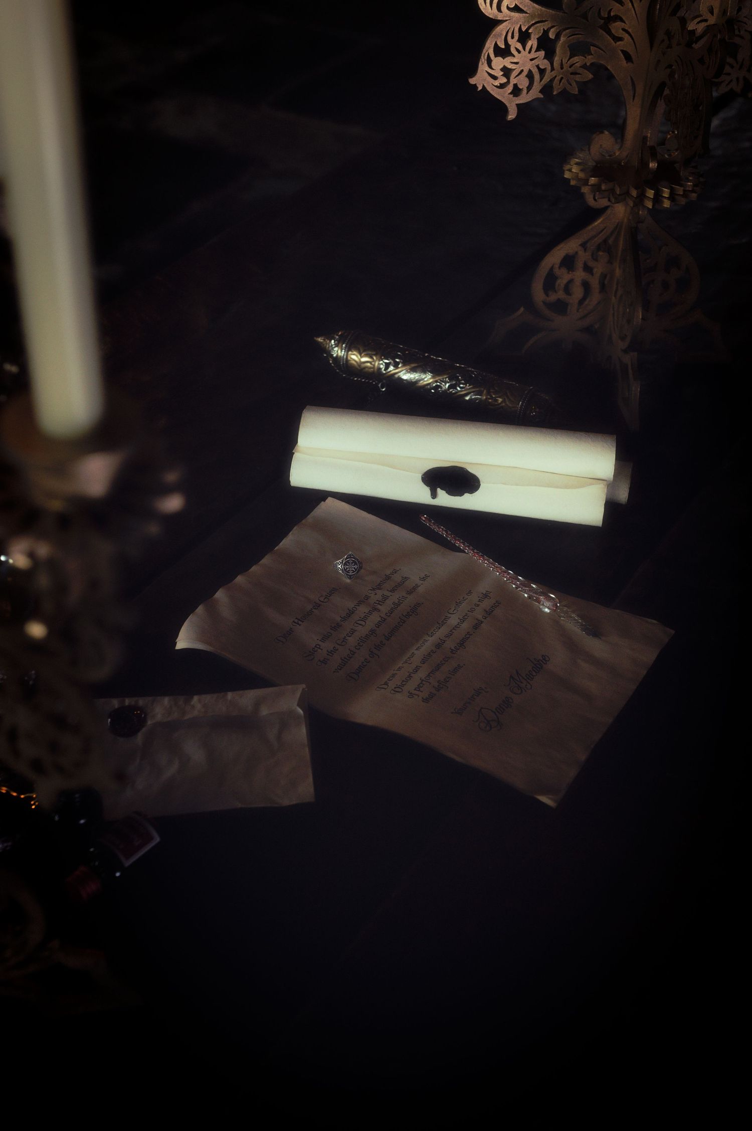 Dark gothic flat lay with wax-sealed scroll, ornate pen, candle, and vintage papers on black velvet surface.