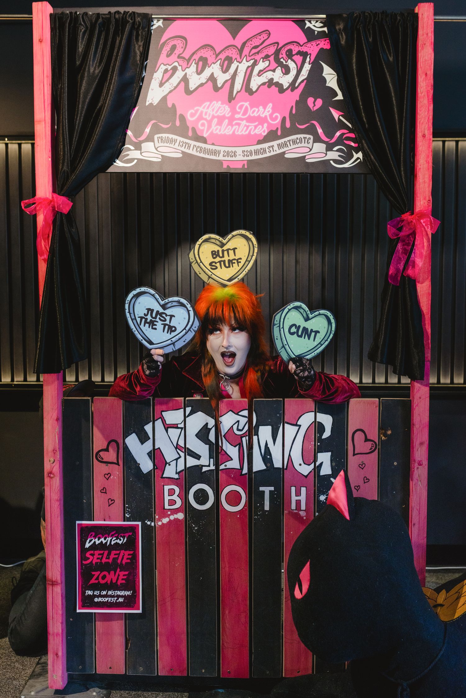 Person posing in a colorful Hissing Booth at Boofest, an alternative dark Valentine's event, holding heart-shaped props.