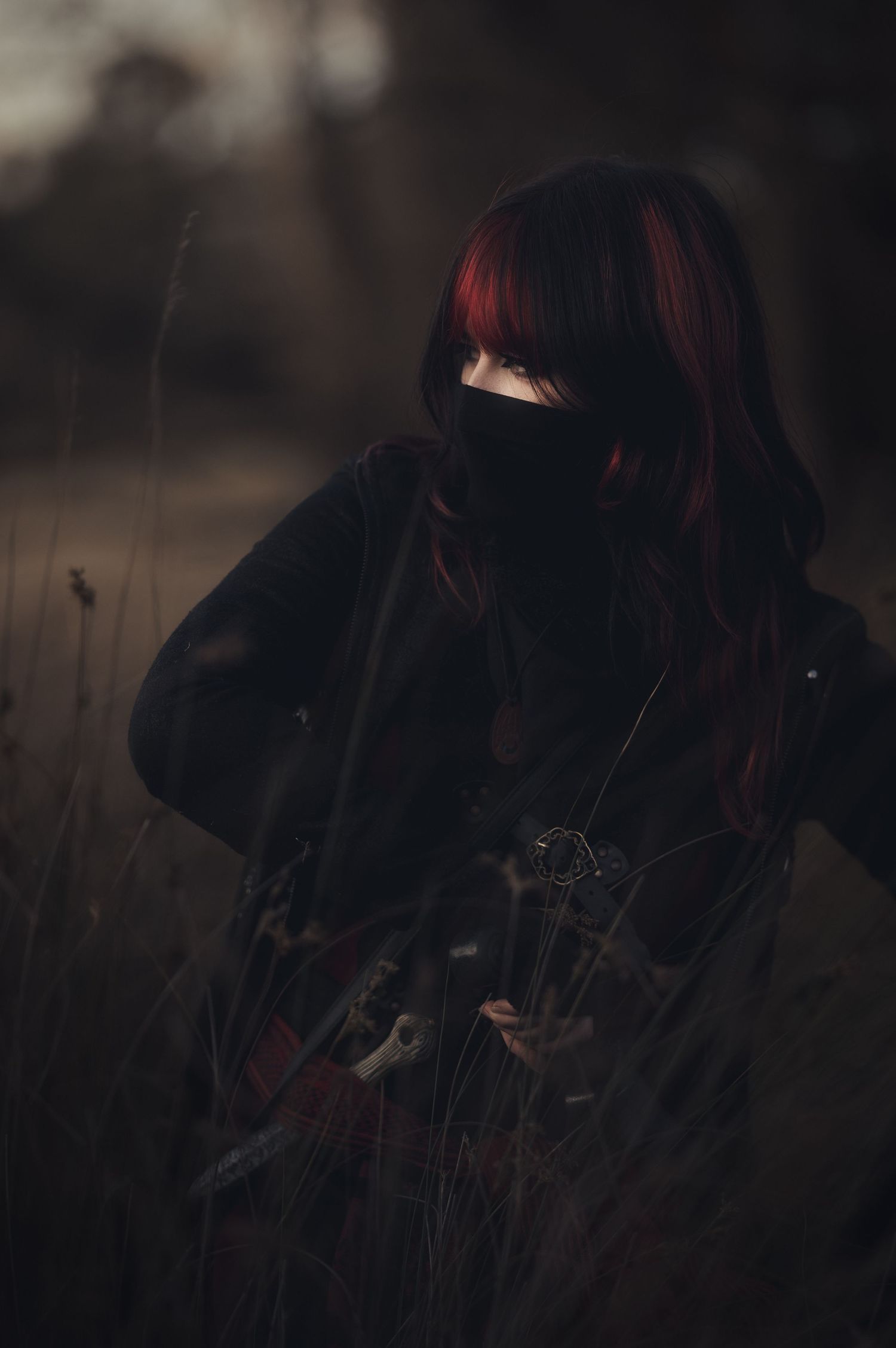 Moody dark photography with figure in black clothing among tall grass.