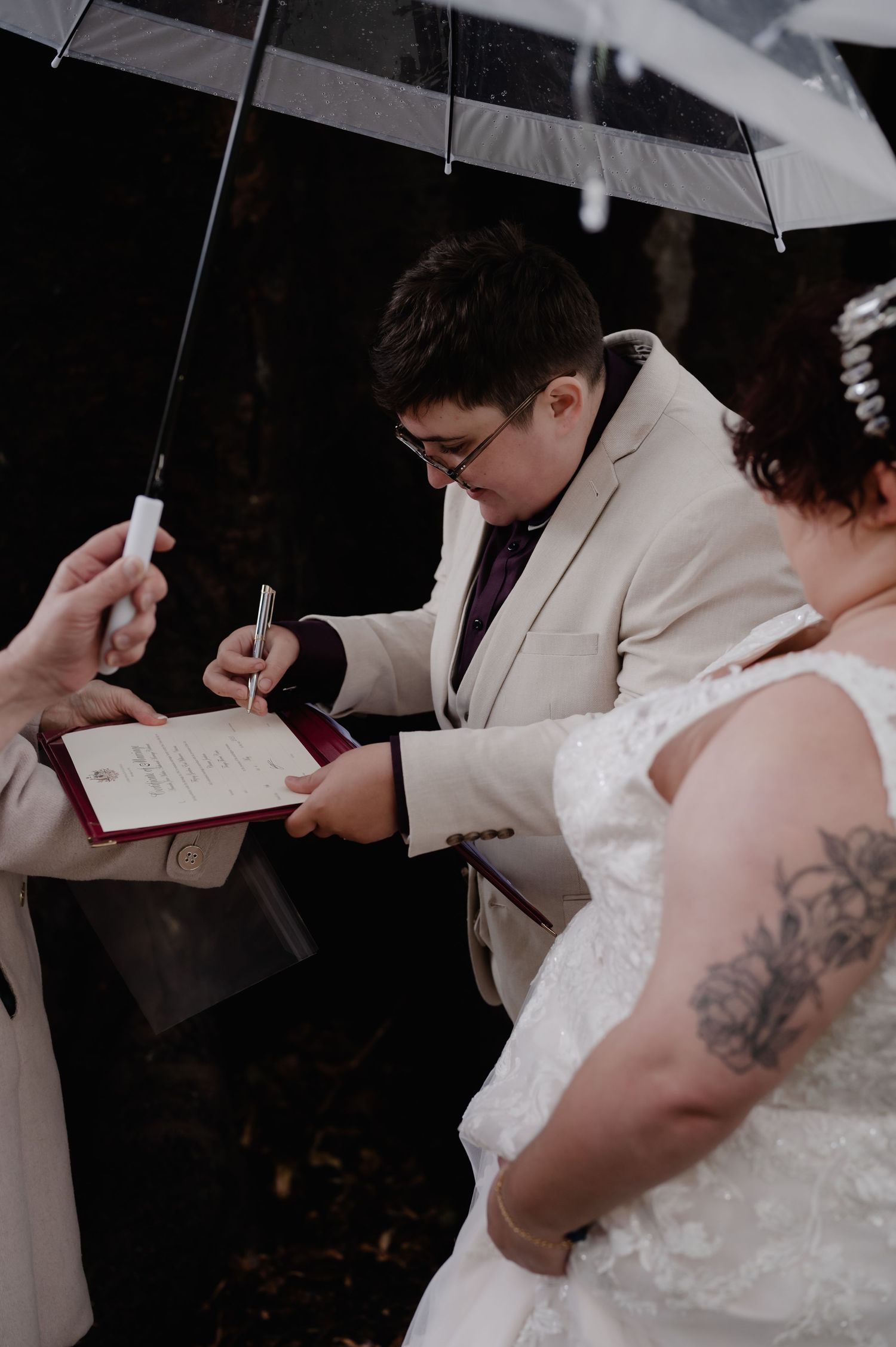 Couple signing wedding documents together under a white umbrella during their ceremony.