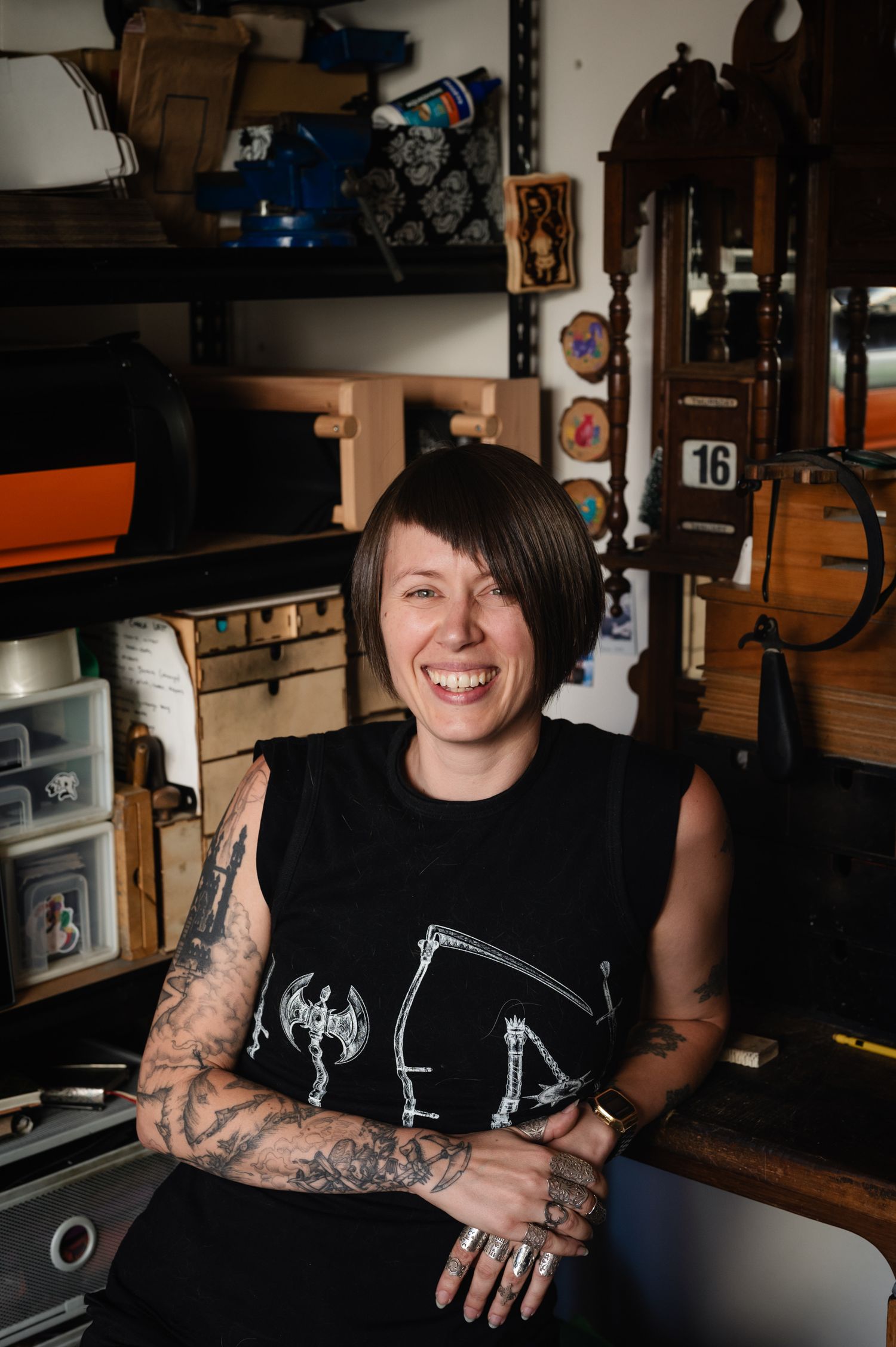 Person in black t-shirt with tattoos smiling in indoor workspace setting.