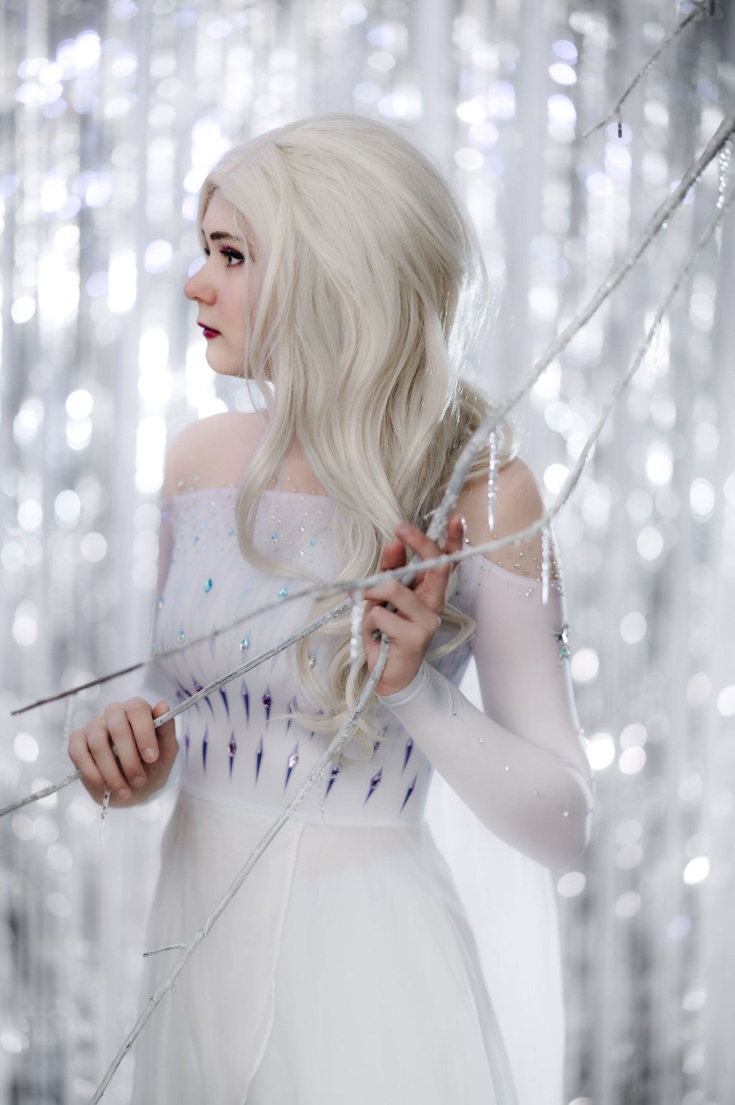Artistic fashion portrait with platinum hair and white gown against glittering background.