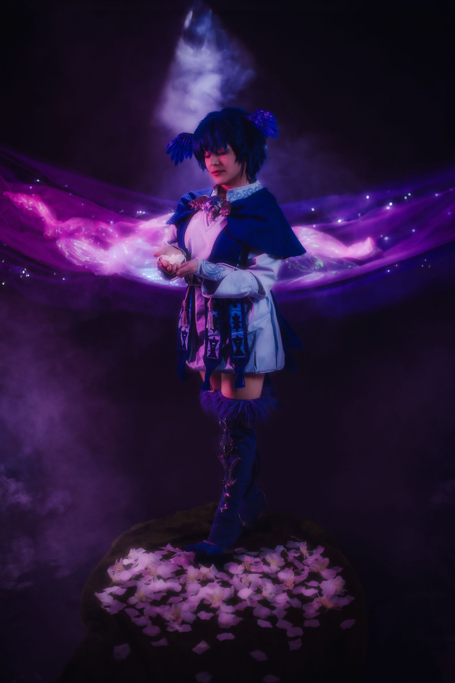 A person in a blue jacket poses with magical purple smoke effects and scattered flower petals in a dark setting.