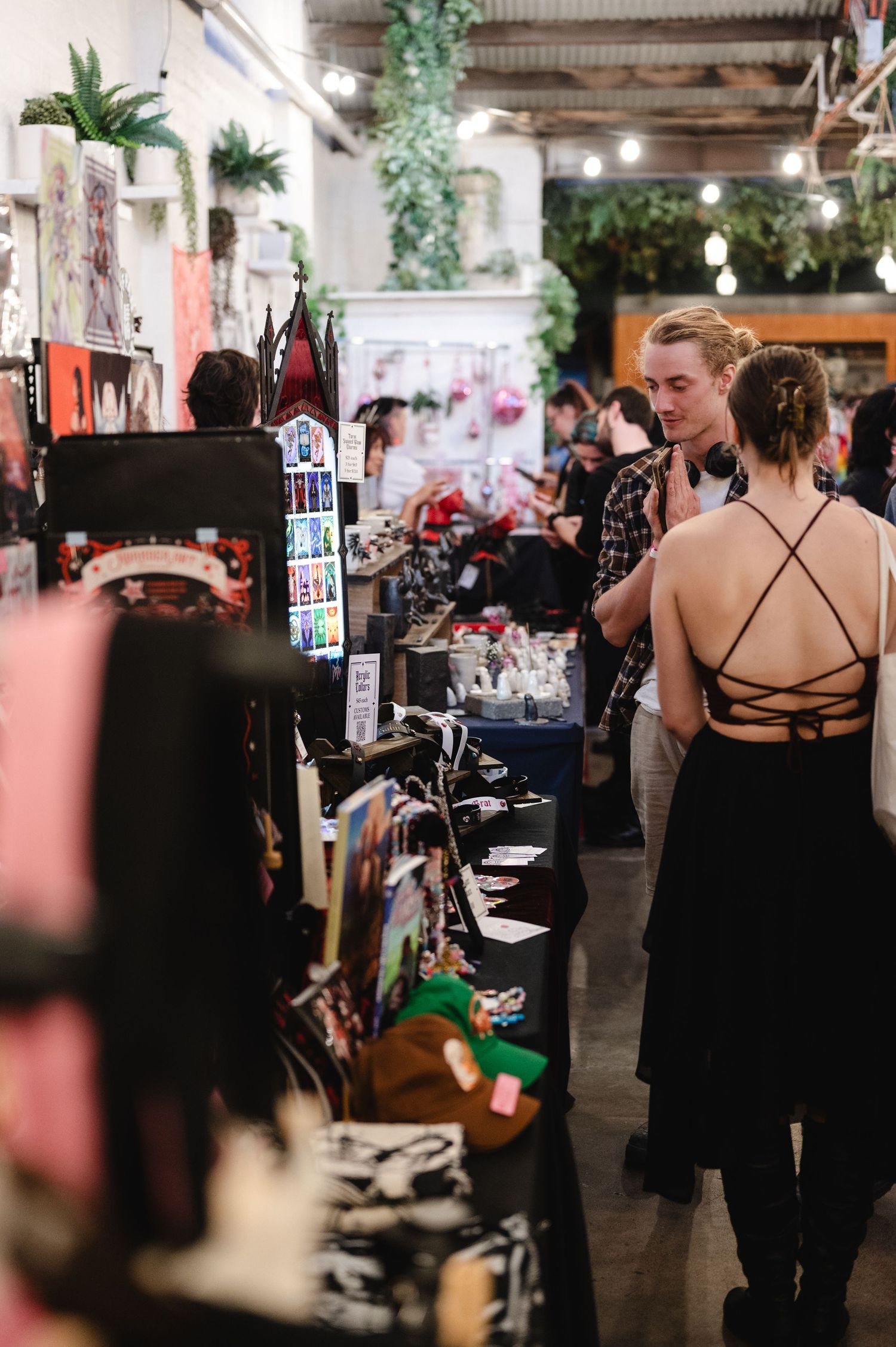 People browse vendor tables and displays at an indoor market or craft fair event.