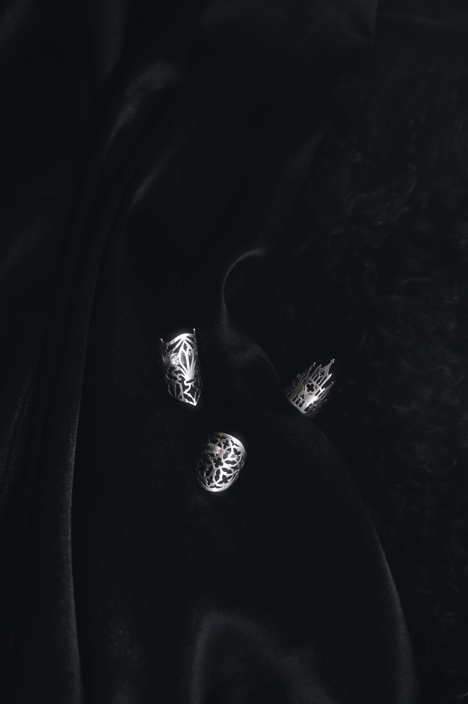 Three ornate silver rings photographed against a black velvet background with smoke effects.