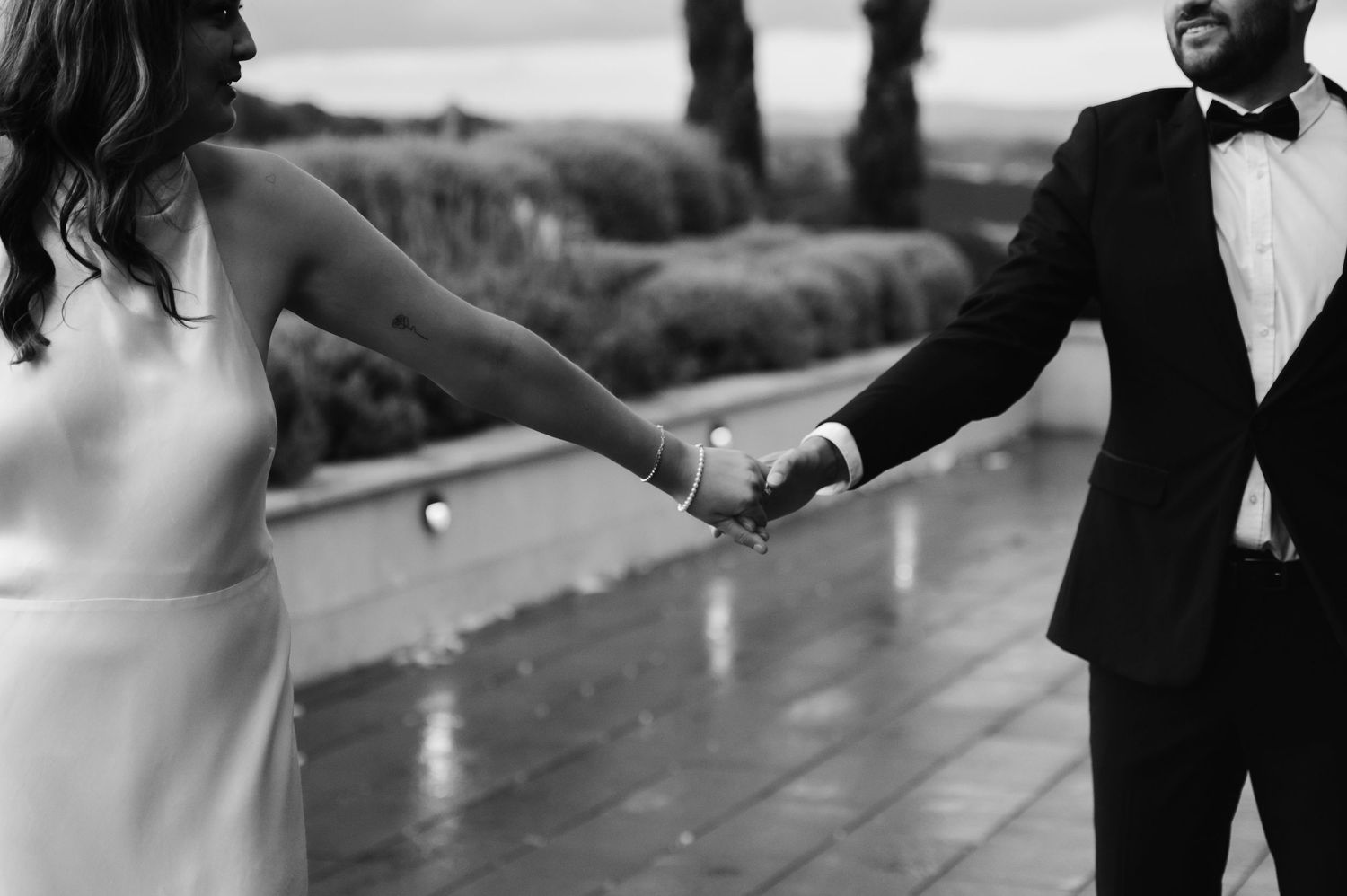 Couple holds hands while dancing on outdoor patio during sunset celebration.