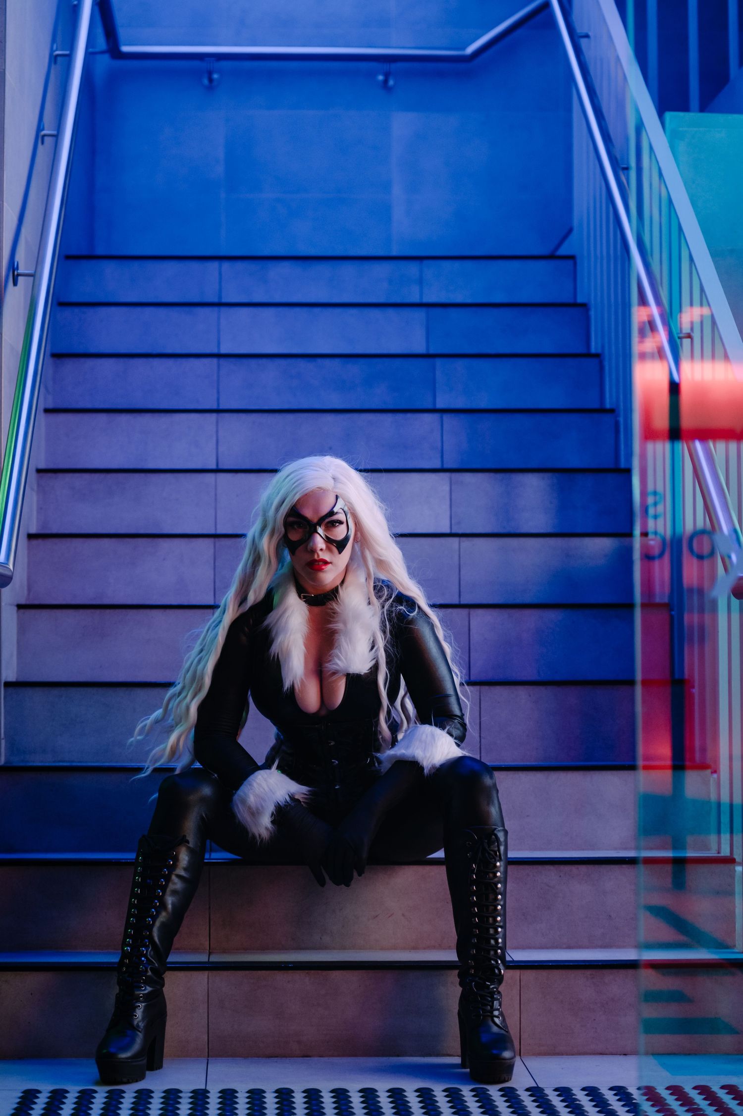 Moody Black Cat cosplay portrait on blue-lit staircase with neon accents.