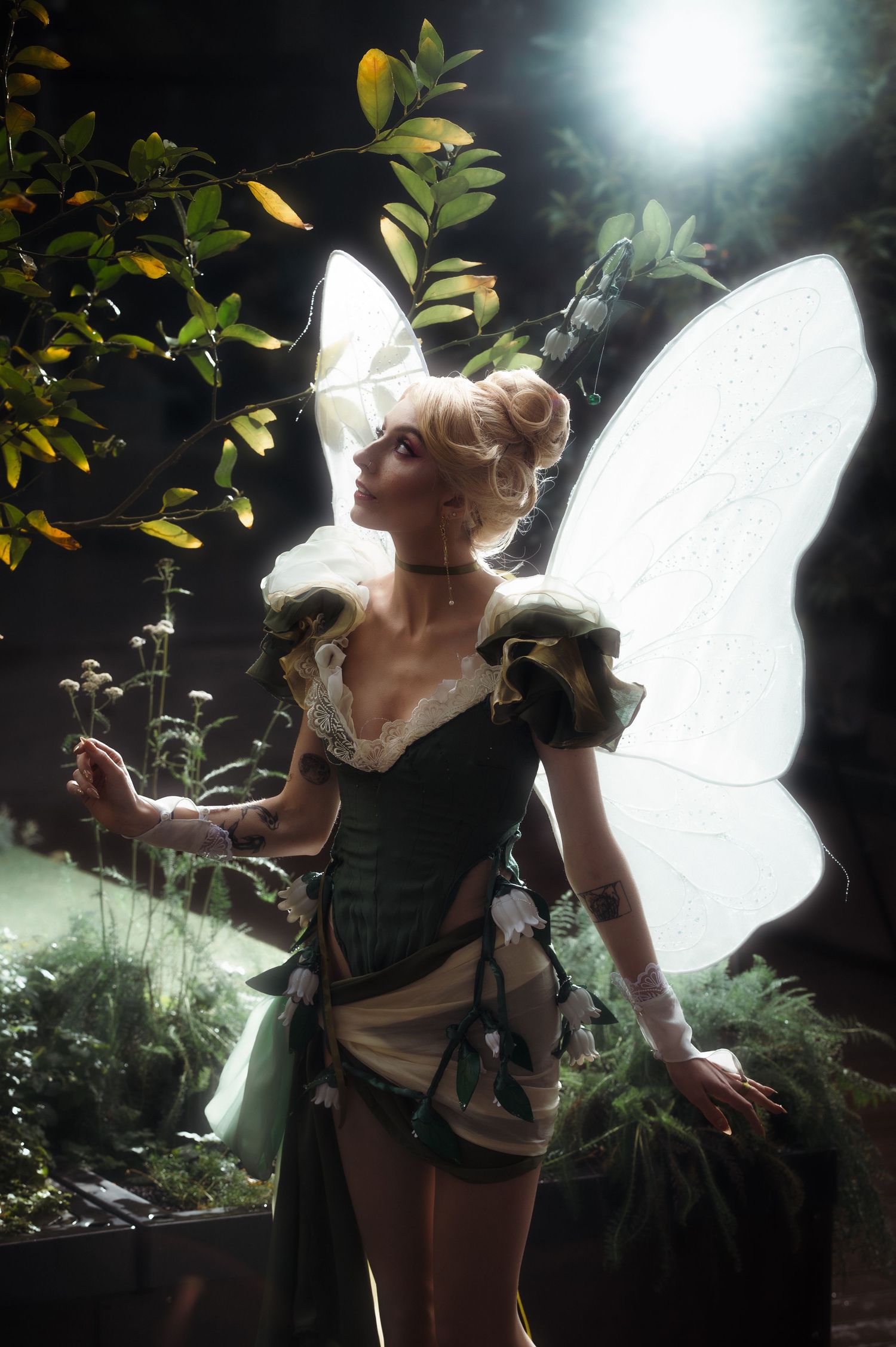 Fantasy fairy costume photoshoot with illuminated wings in dark forest setting.
