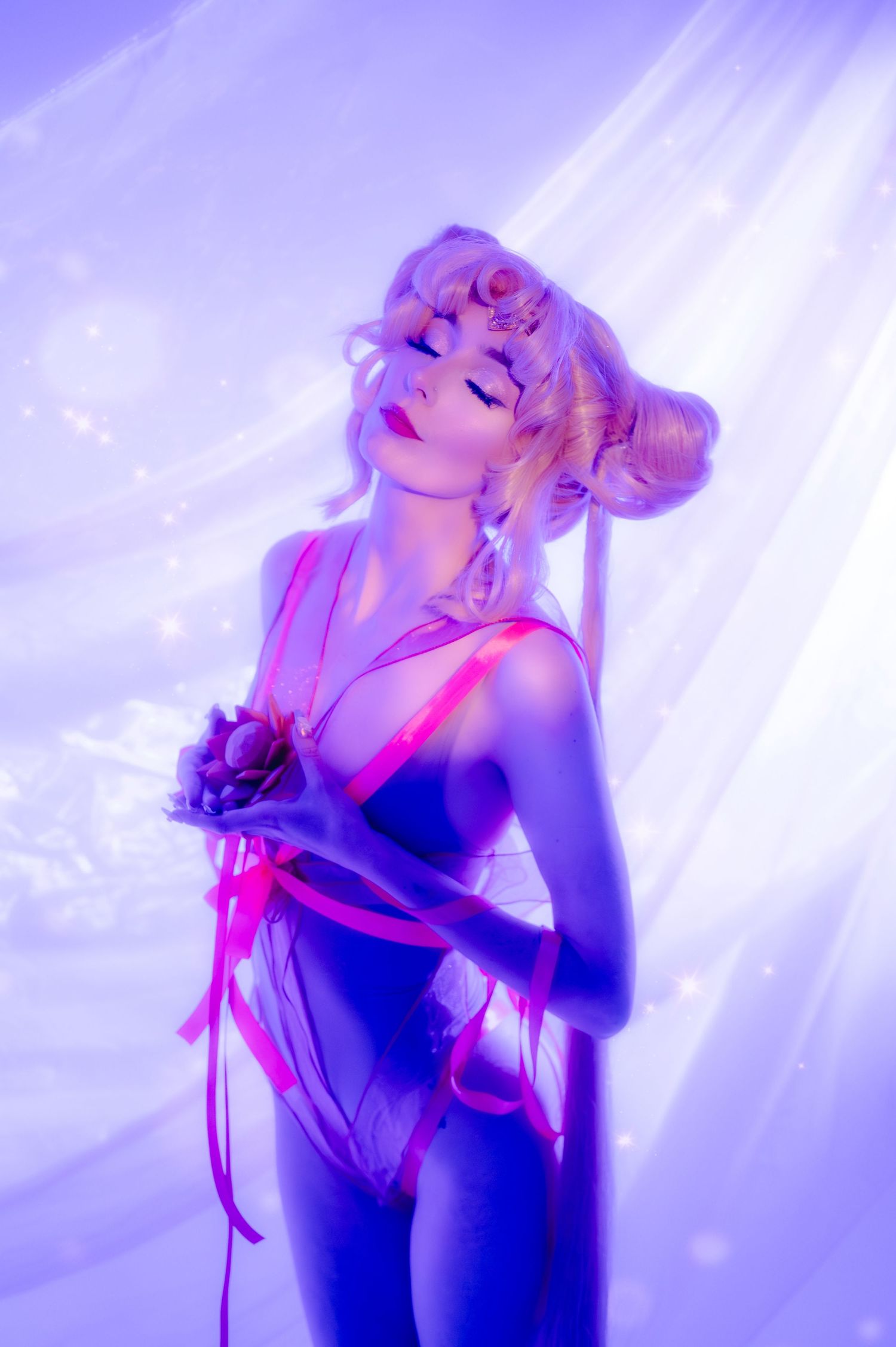A cosplayer in a purple-lit scene wearing a pink ribbon bodysuit with blonde twin buns hairstyle poses gracefully.