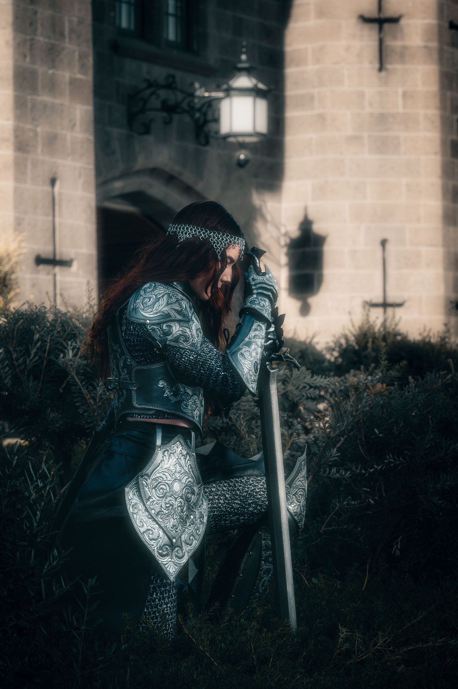 Medieval knight in ornate armor and chainmail holds a sword against stone castle walls.