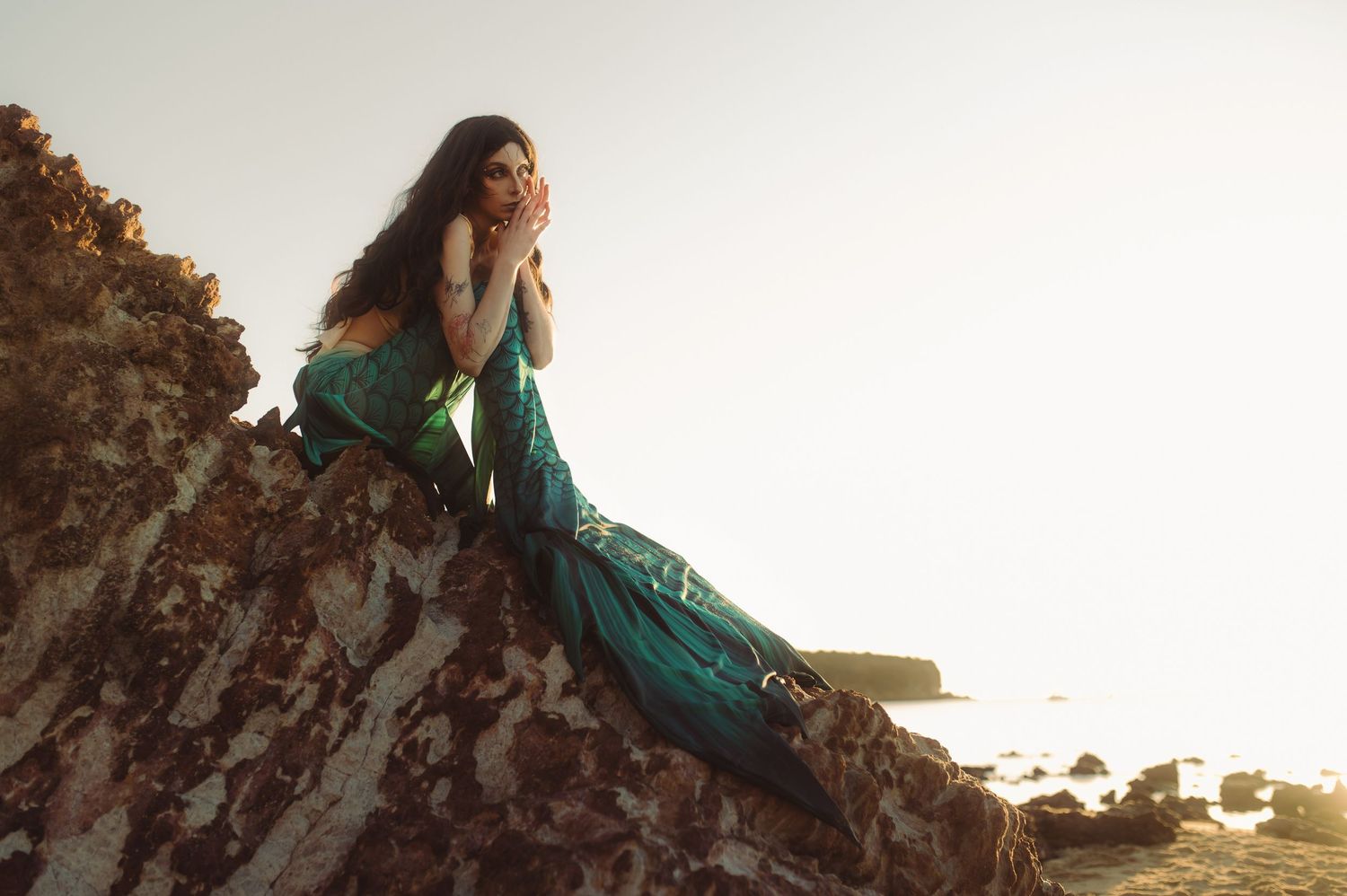 Silhouetted figure in flowing dress poses on rocky cliffs at sunset.