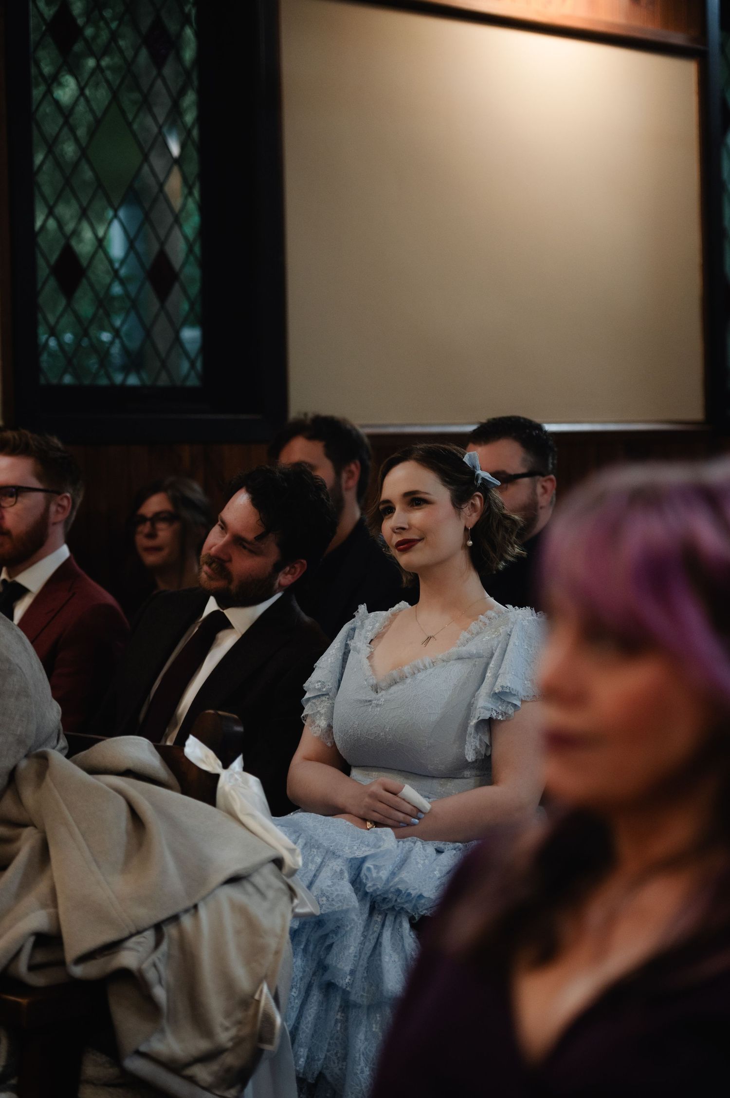Wedding guests seated in formal attire watch ceremony in indoor venue.