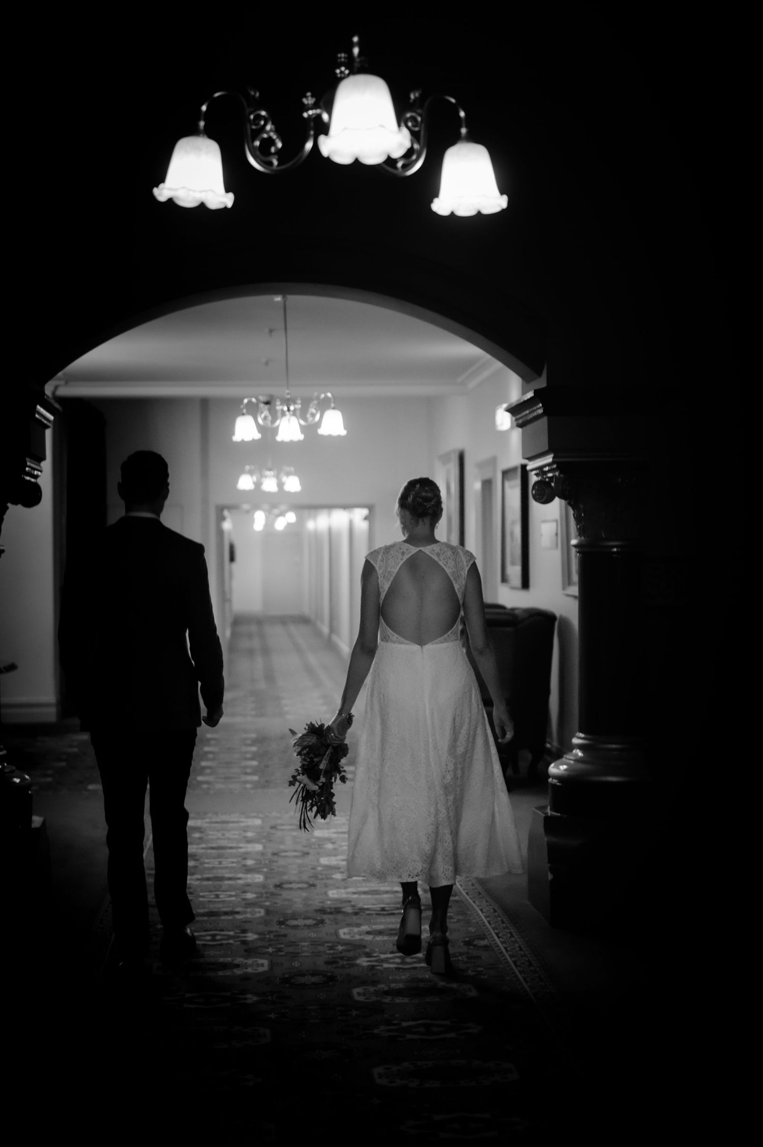 Silhouetted figures walk through an arched hallway with glowing pendant lights.