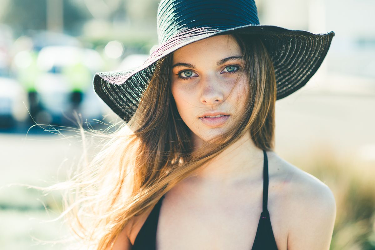 Young woman wearing a wide-brim straw hat with long hair blowing in the wind on a sunny day.