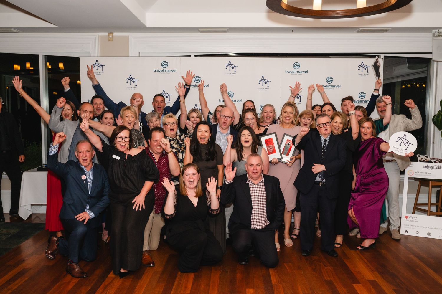 A group of wedding guests raise their arms in celebration during a reception party at an indoor venue.