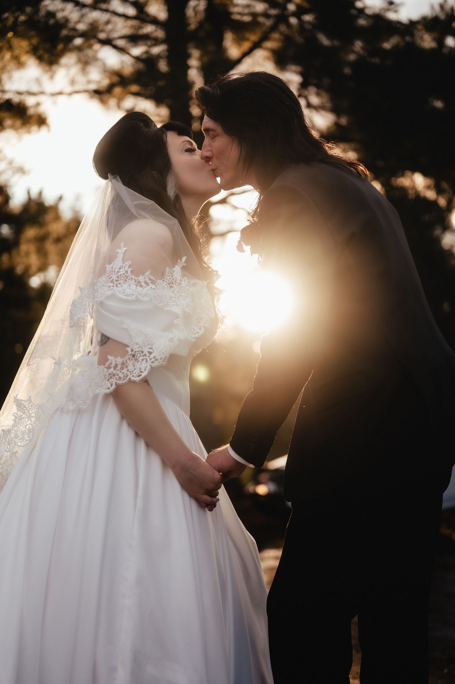 Romantic silhouettes of newlyweds sharing intimate moments at sunset with golden light filtering through trees.