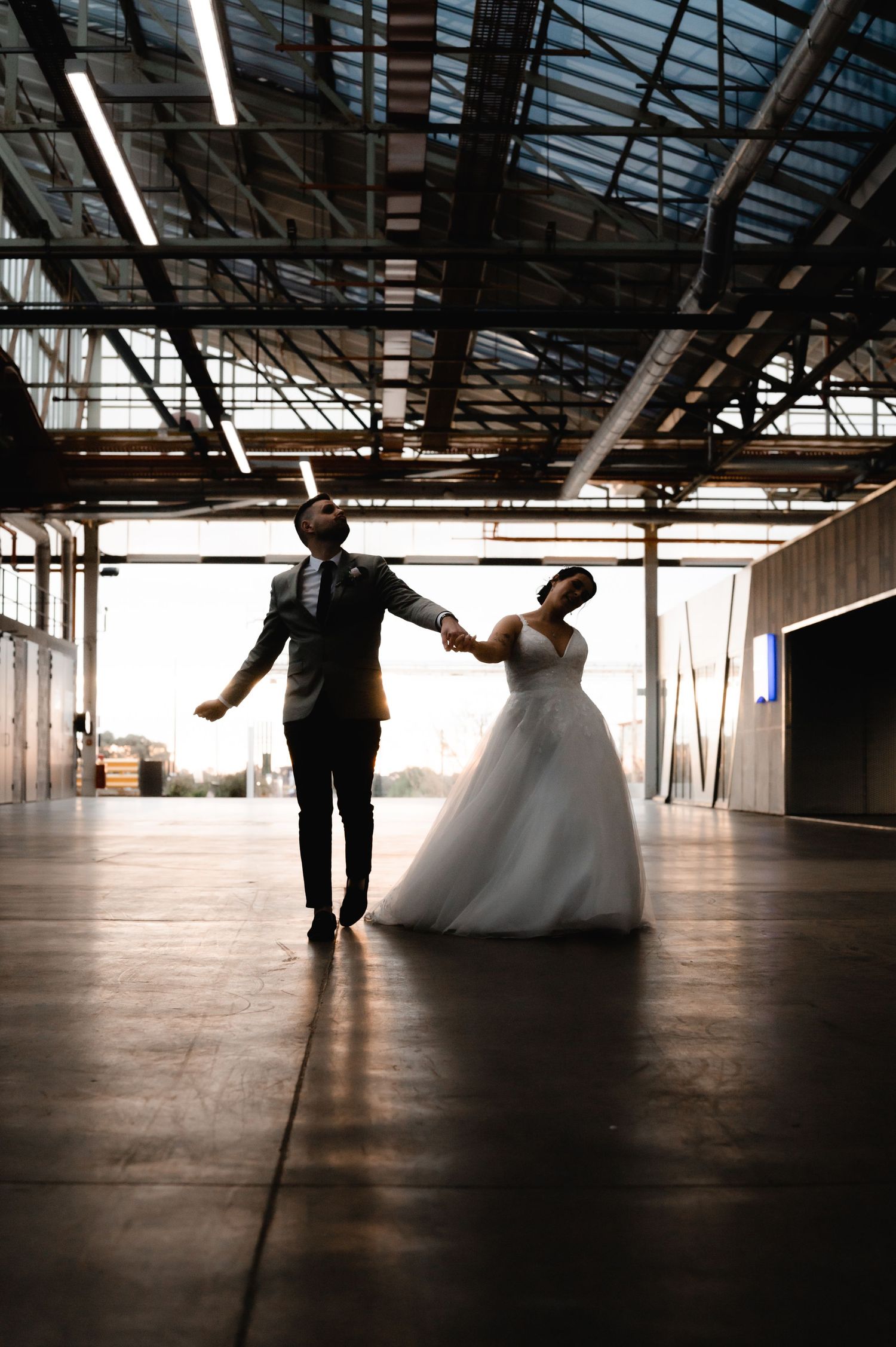 Couple dances together in spacious empty warehouse with dramatic lighting.
