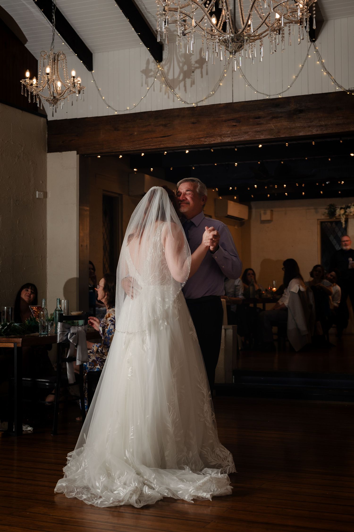 Wedding couple dances under crystal chandeliers in an elegant reception venue.