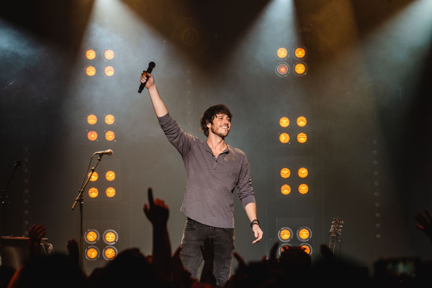 Male performer raises fist on stage at concert with dramatic lighting and crowd cheering below.