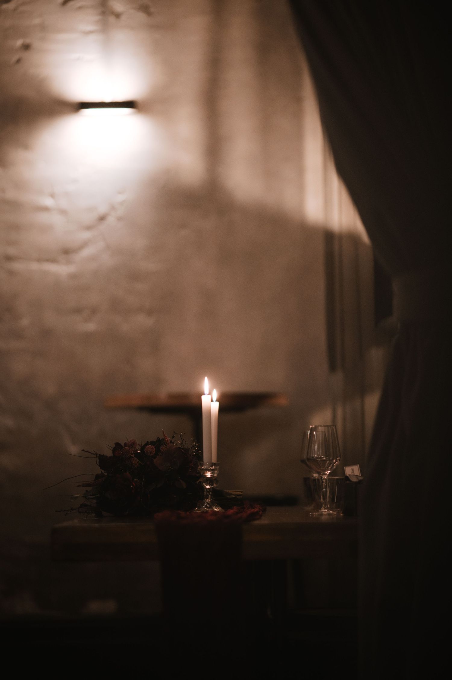 Moody candlelit table setting with glowing ambient light and wine glasses.