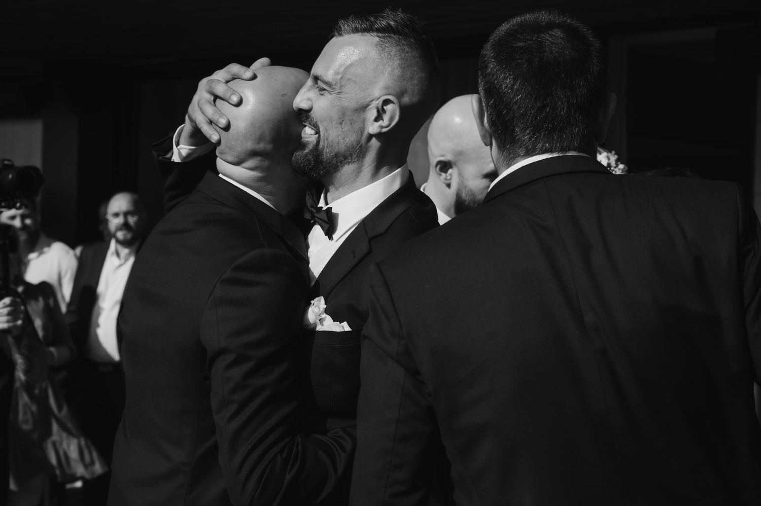 Black and white candid shot of wedding guests sharing laughter and embraces.