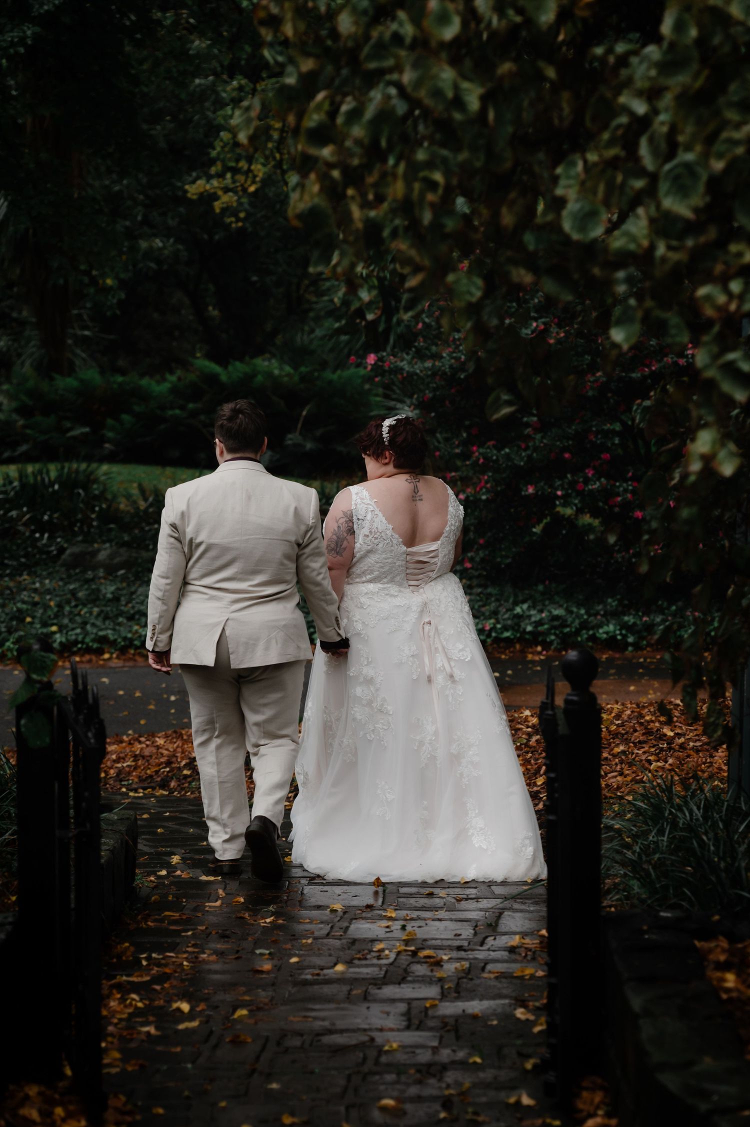 A newlywed couple walking together on a stone path surrounded by autumn foliage.