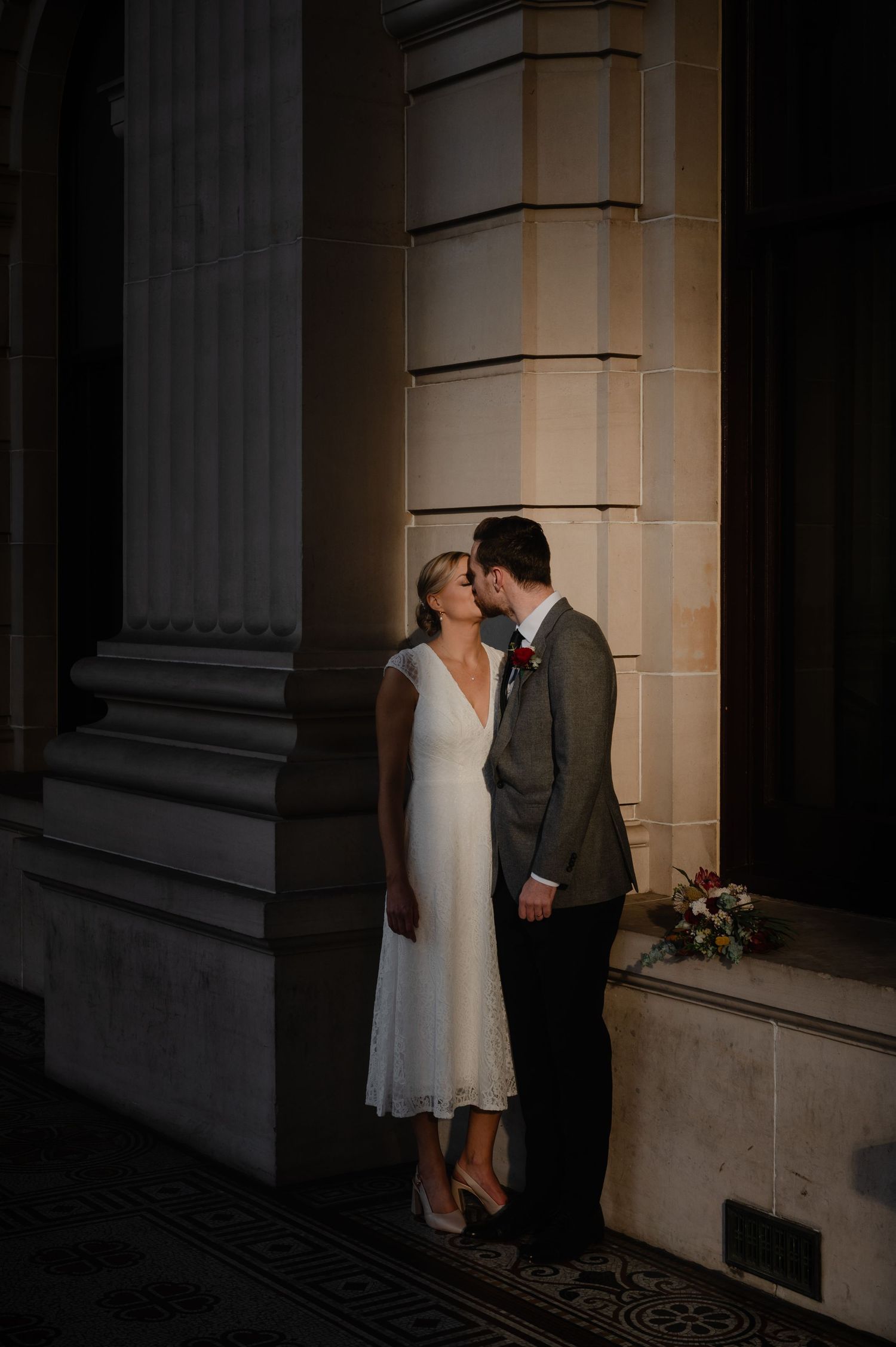 Intimate moment between couple against stone columns with dramatic shadows.