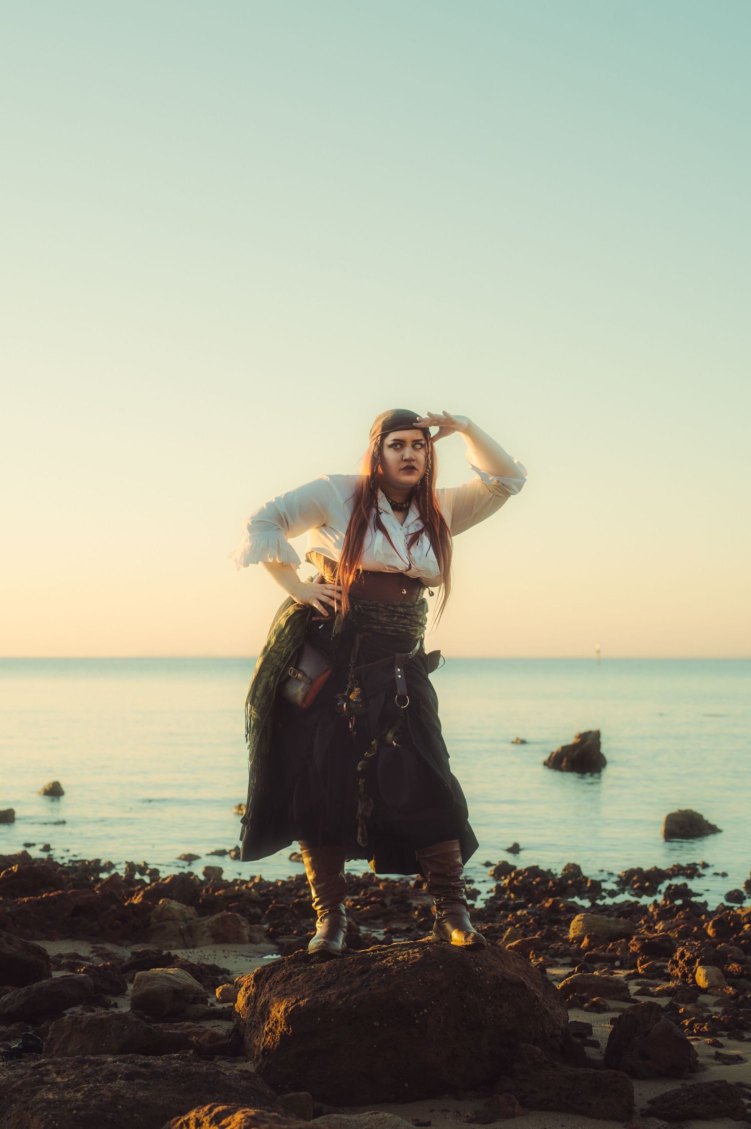 Coastal photoshoot at golden hour with rocks and calm ocean in background.
