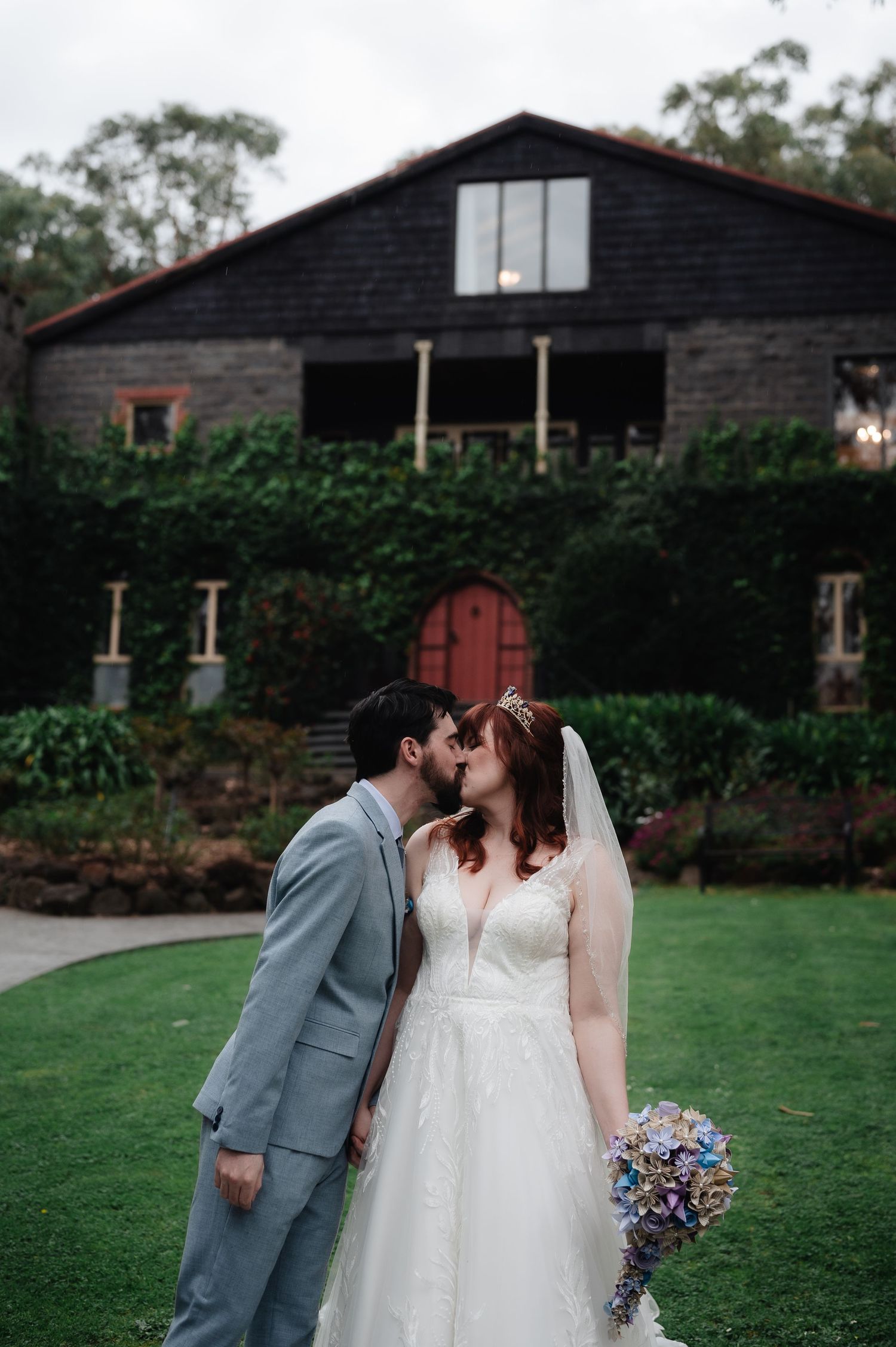 Romantic wedding portrait of couple sharing a kiss in front of charming barn venue.