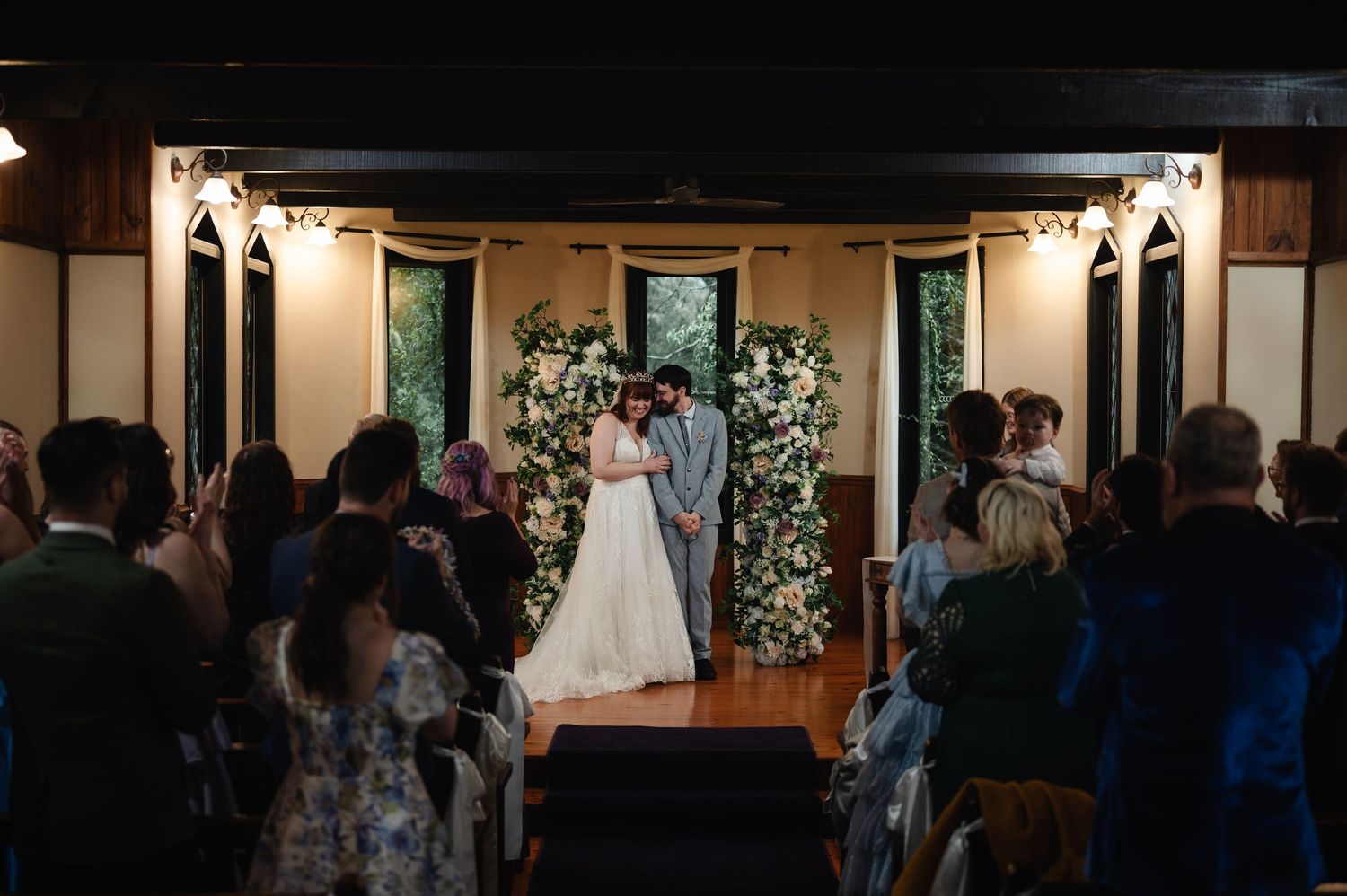 Wide shot of wedding ceremony in rustic indoor venue with exposed beams and natural light.