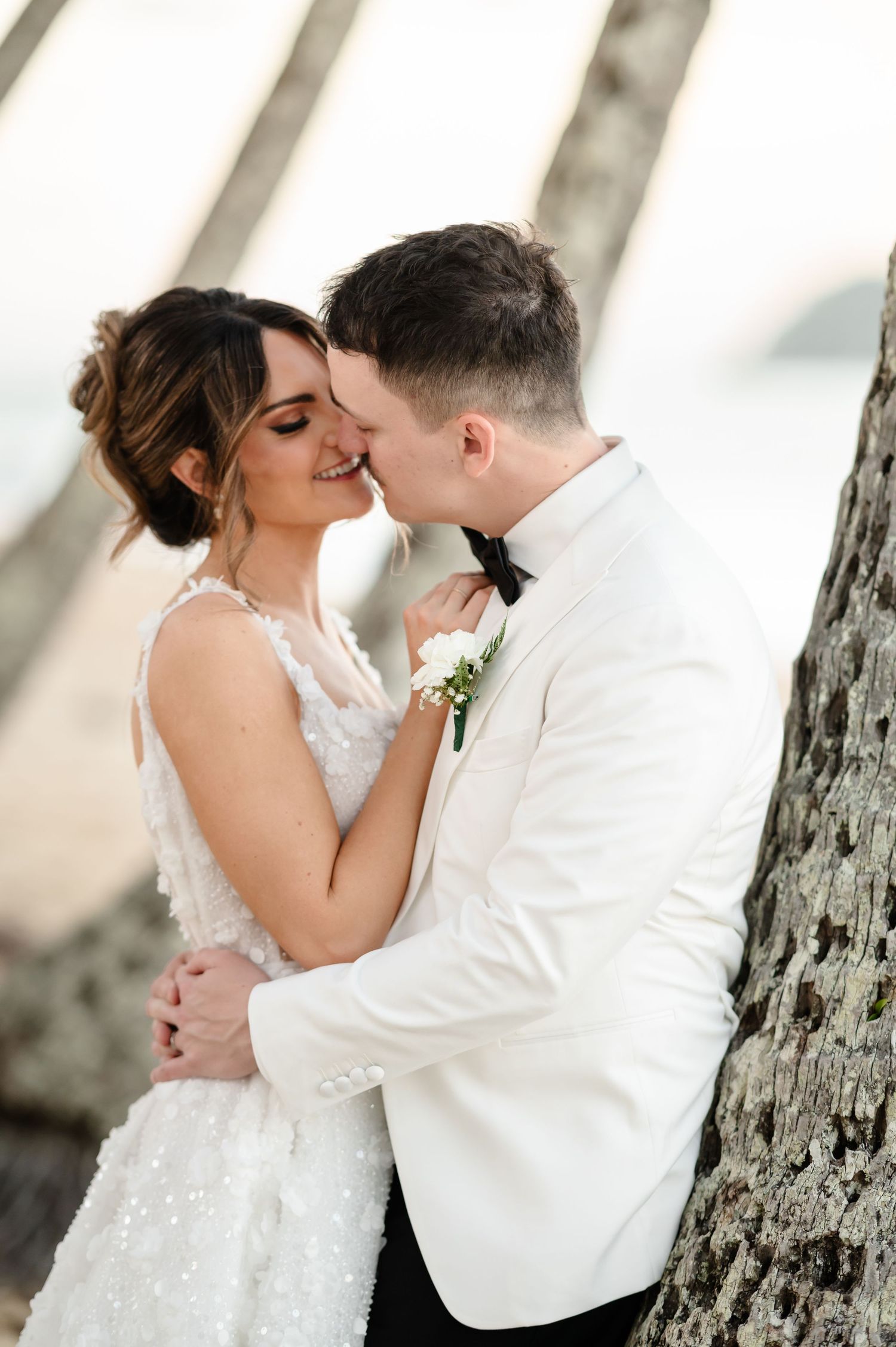 Romantic wedding couple embraces against a tree trunk in a dreamy outdoor setting.