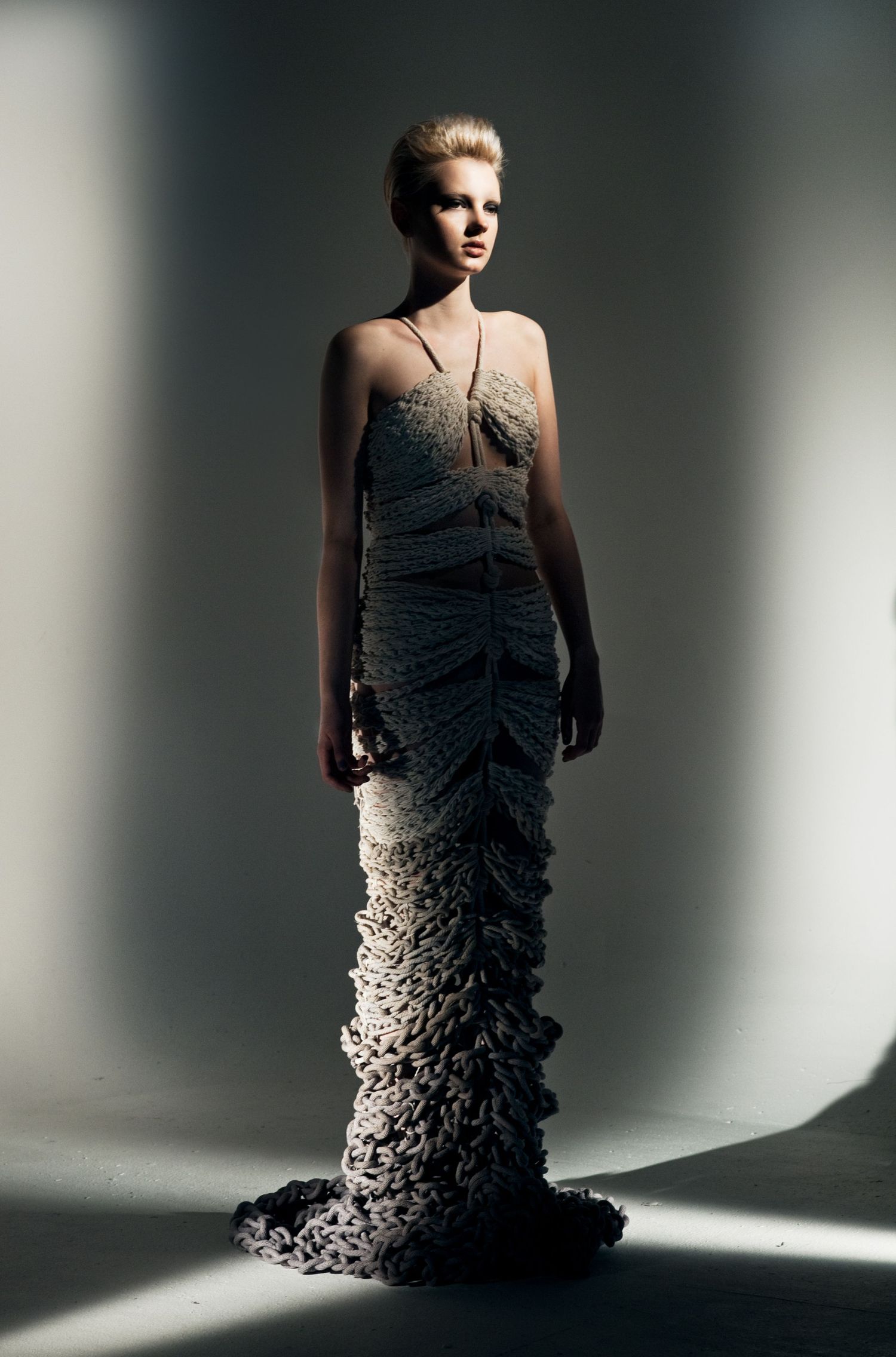 A model poses in an avant-garde textured gown with ruffled hem details under dramatic studio lighting.