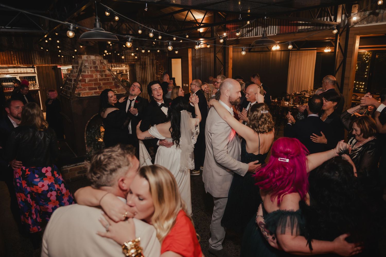 Guests dancing and celebrating at a dimly lit indoor wedding reception.