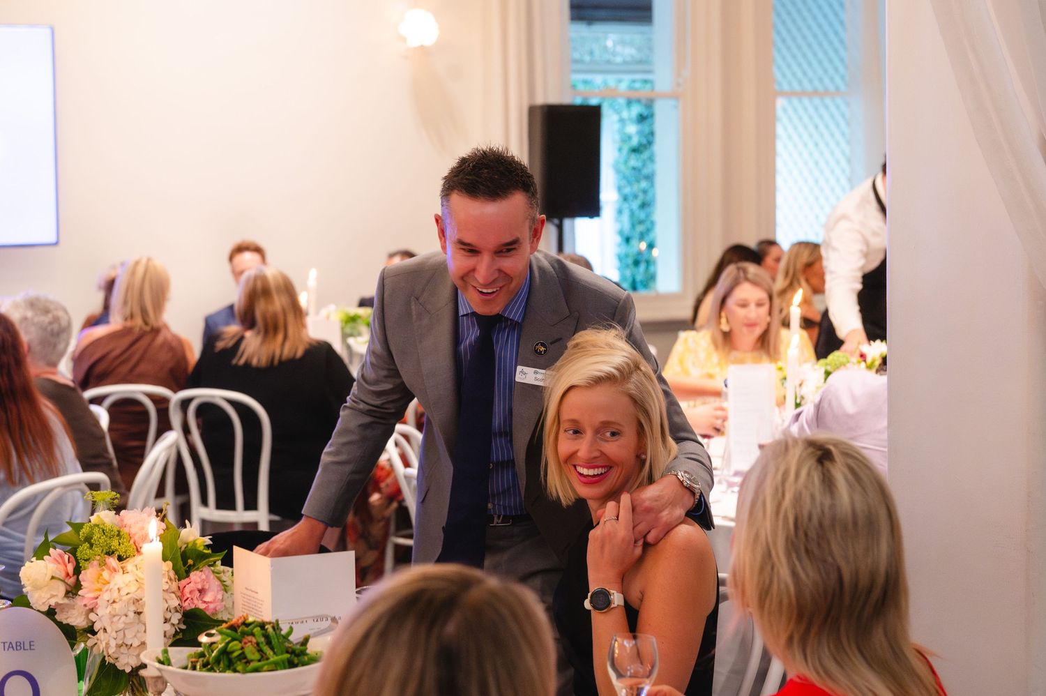Wedding guests enjoy a lively reception celebration at an indoor venue with elegant table settings and decor.