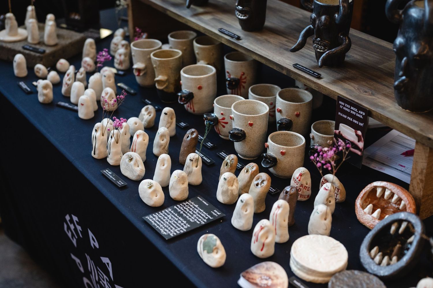 Display of handcrafted ceramic figurines and pottery pieces arranged on dark tables at a craft market.