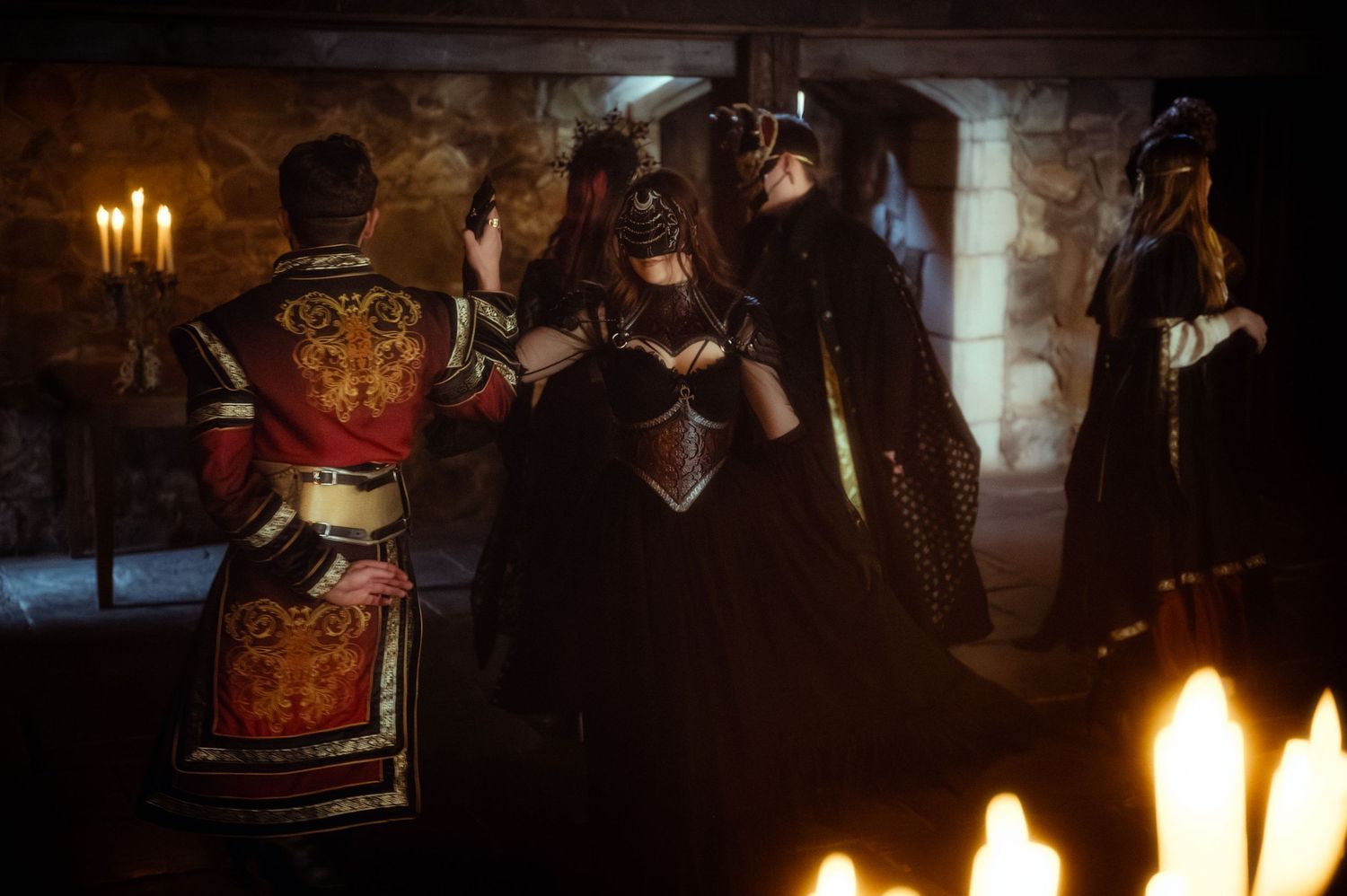 Medieval fantasy scene with costumed figures in dark robes and masks gathered by candlelight in a stone chamber.