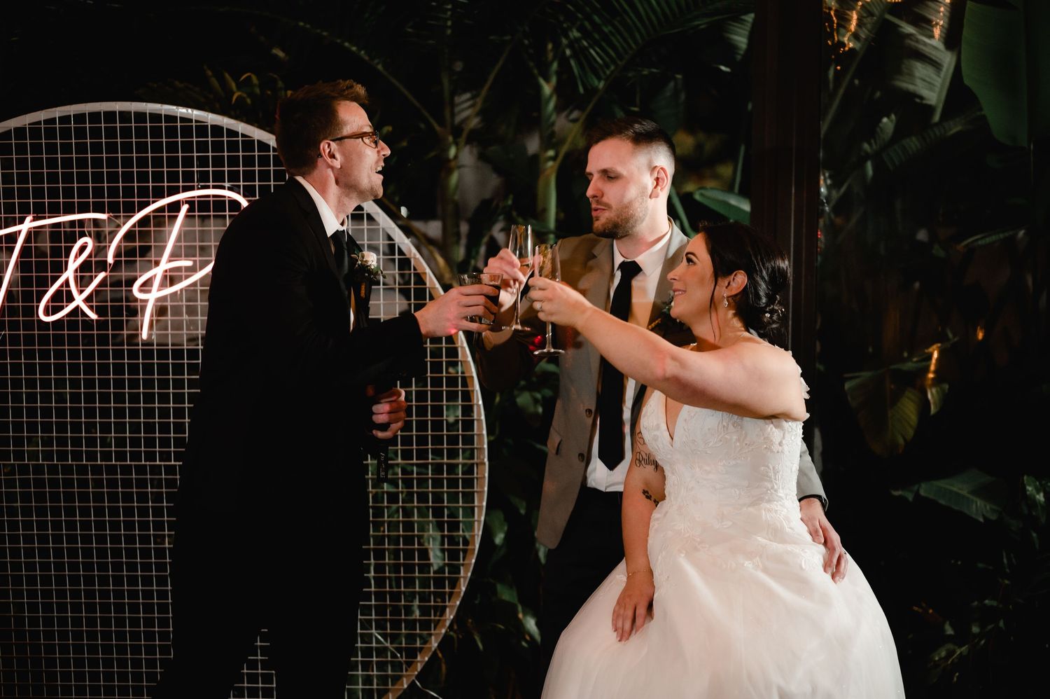 Wedding party dancing energetically in a dark reception venue with decorative lighting.