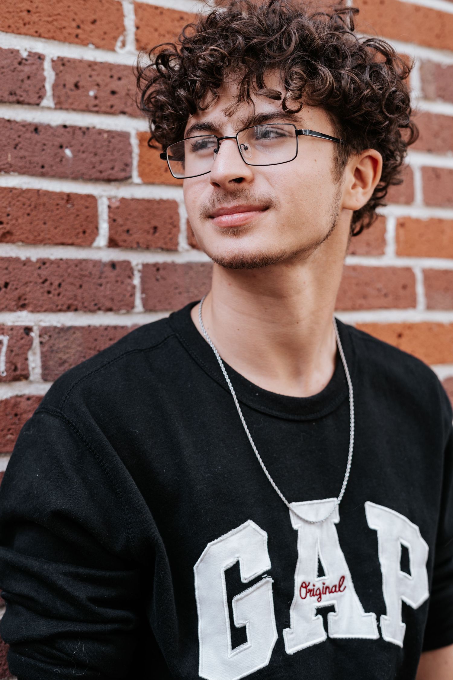 Person in black t-shirt with white text and glasses poses against brick wall in downtown lakeland at Lake Mirror.