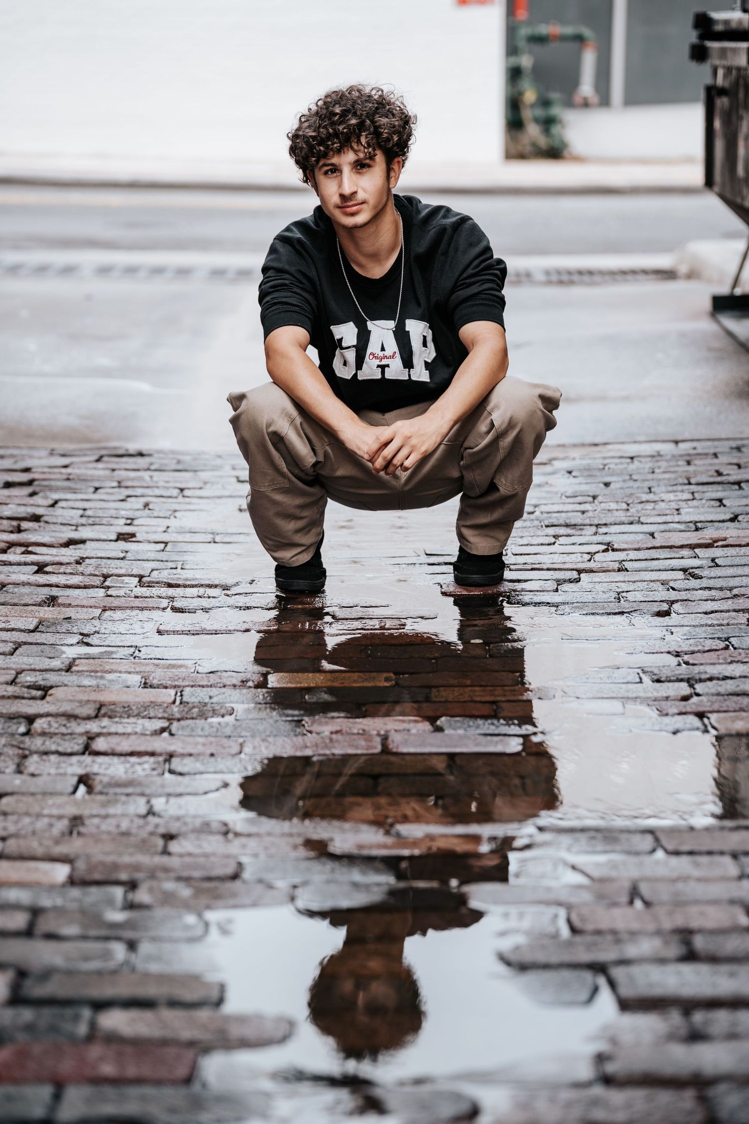 Artistic reflection in puddle on brick pavement shows person crouching in black t-shirt and brown pants in downtown lakeland at Lake Mirror.